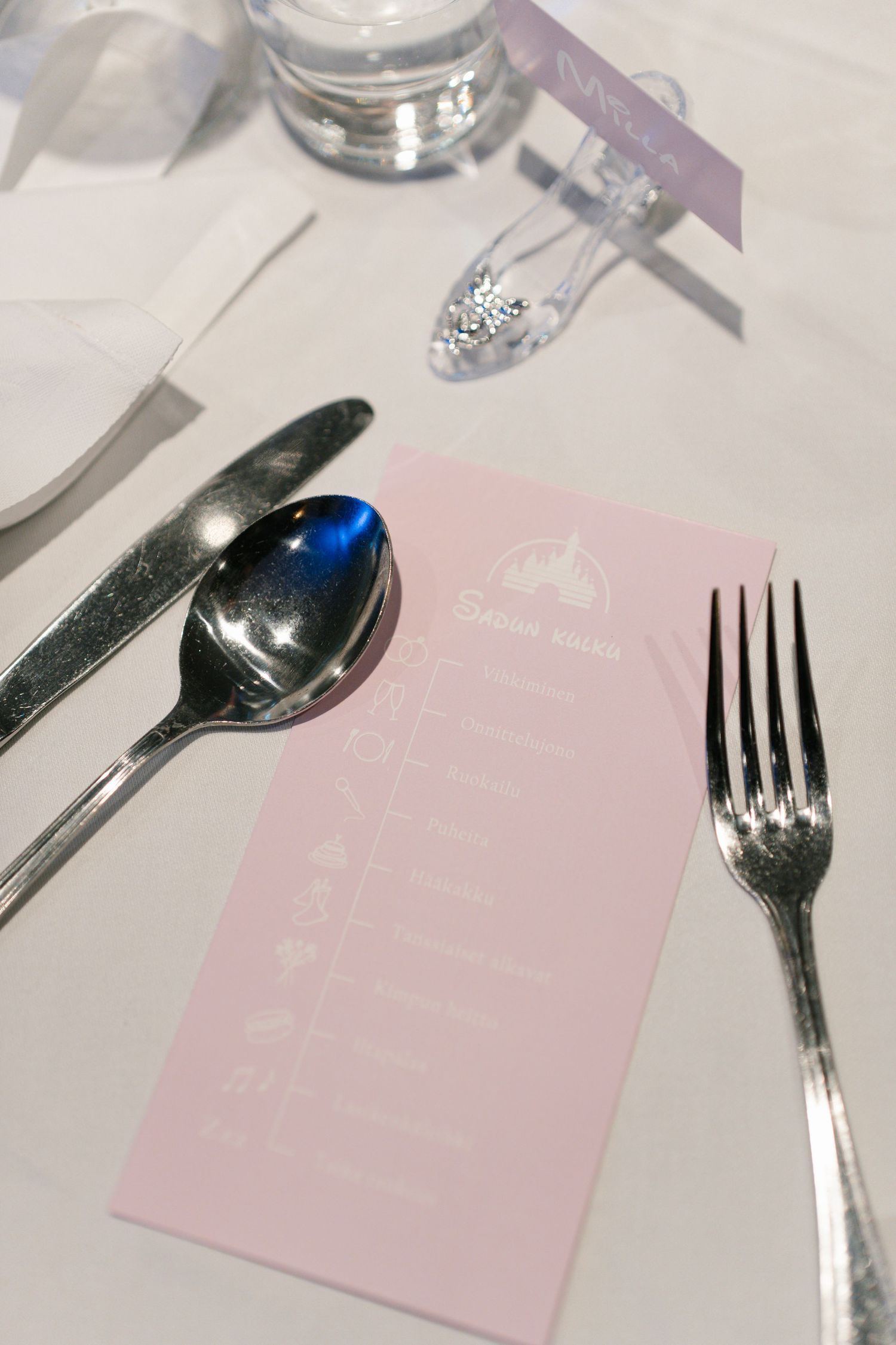 Close-up of pink place cards and silverware on a white tablecloth at a wedding reception.