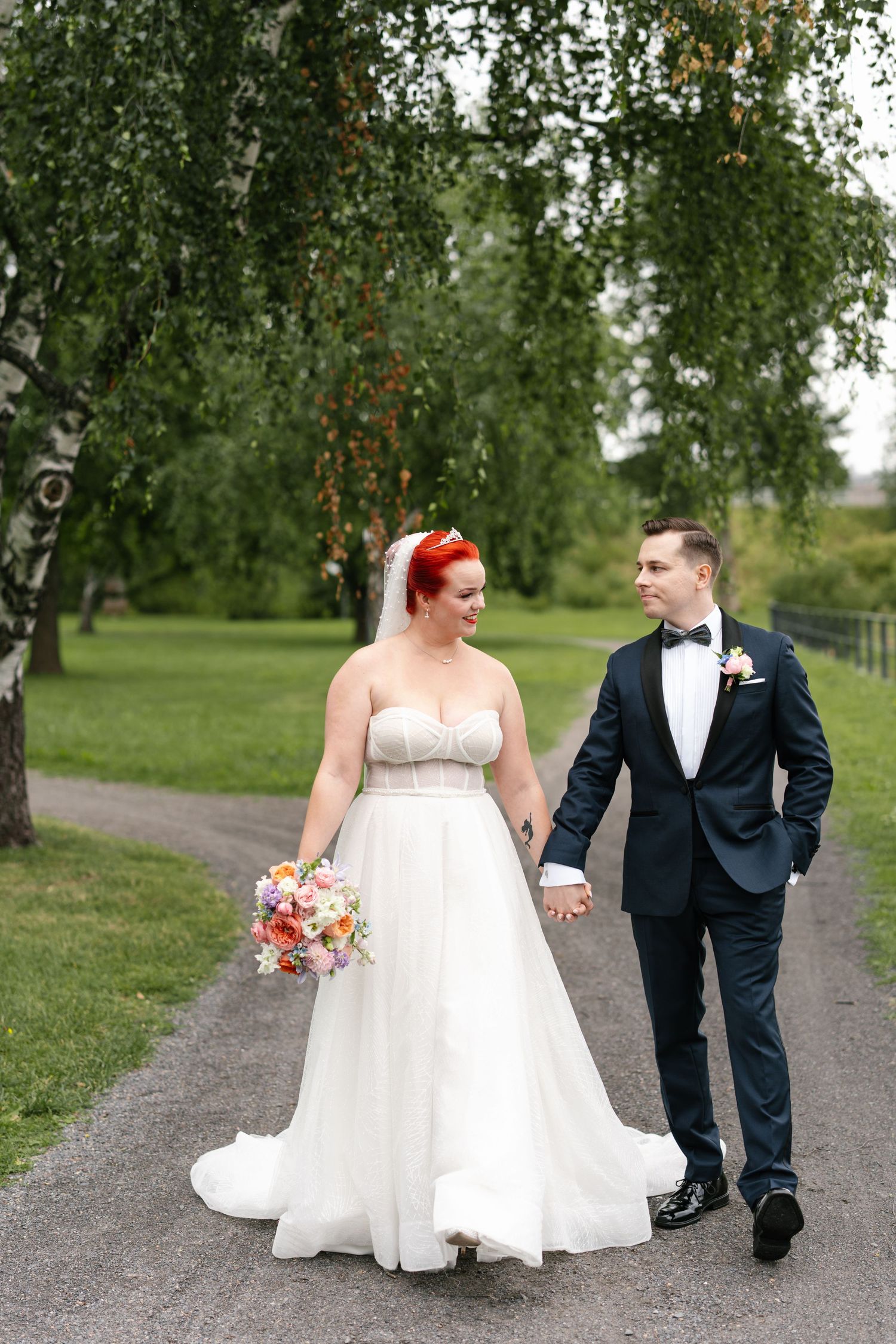 Wedding couple walking along tree-lined path in outdoor garden setting.