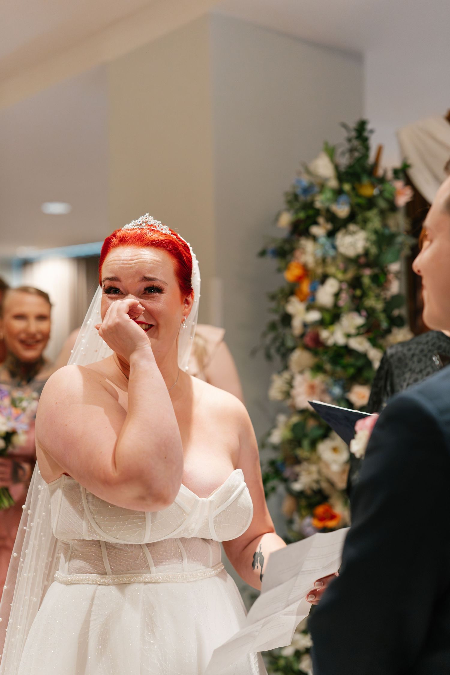 Emotional wedding ceremony moment captured in front of floral arrangements.