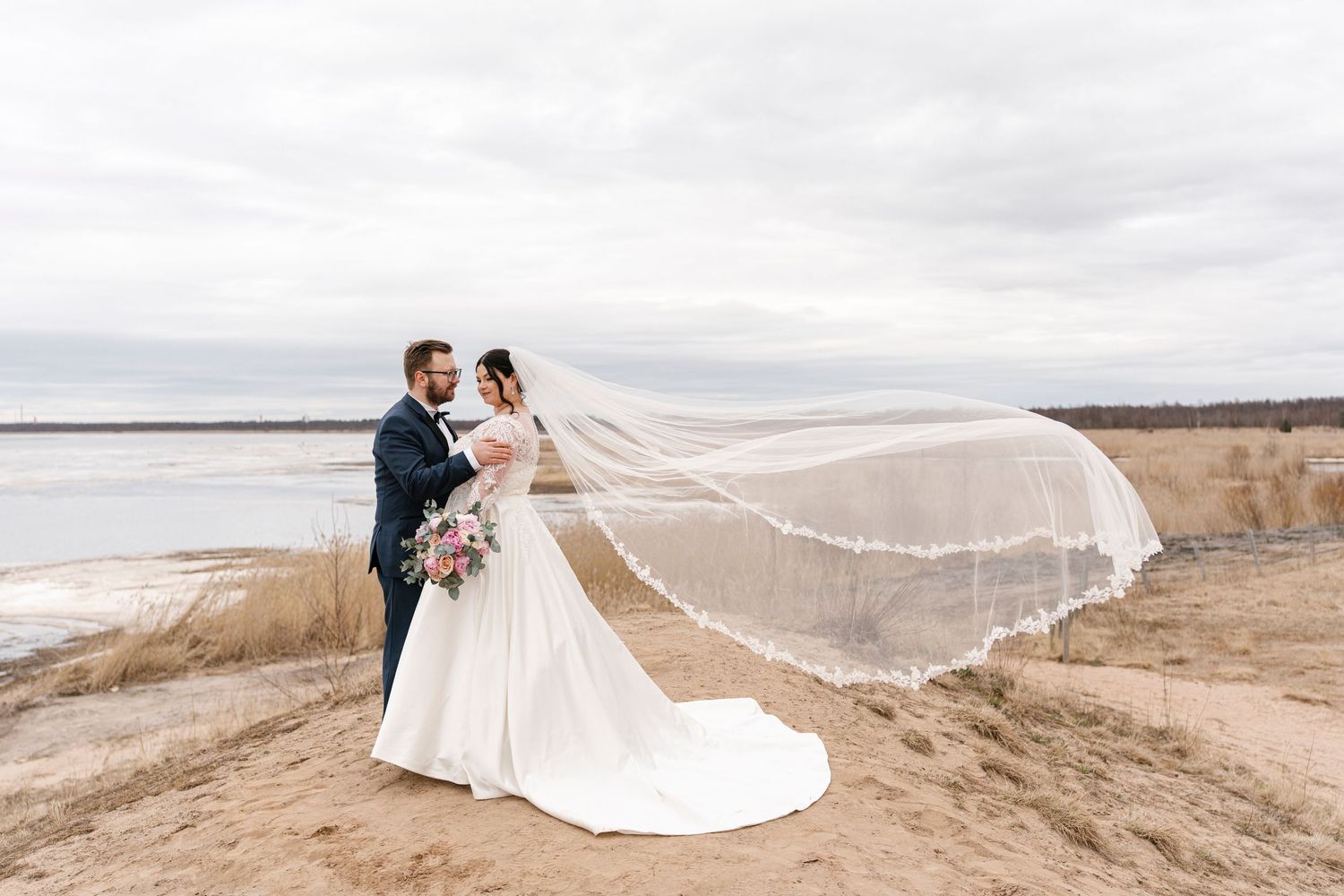 Dramatic wedding photos on a beach with flowing veil catching the coastal breeze.