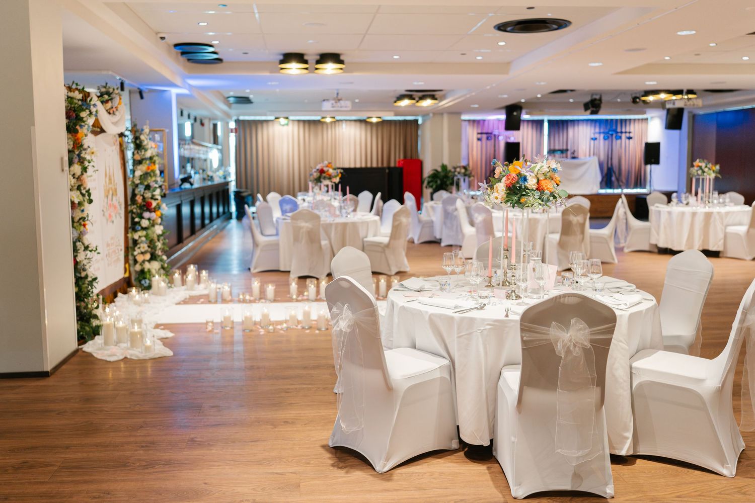 Spacious wedding venue with white-covered chairs and elegant table settings under modern lighting.