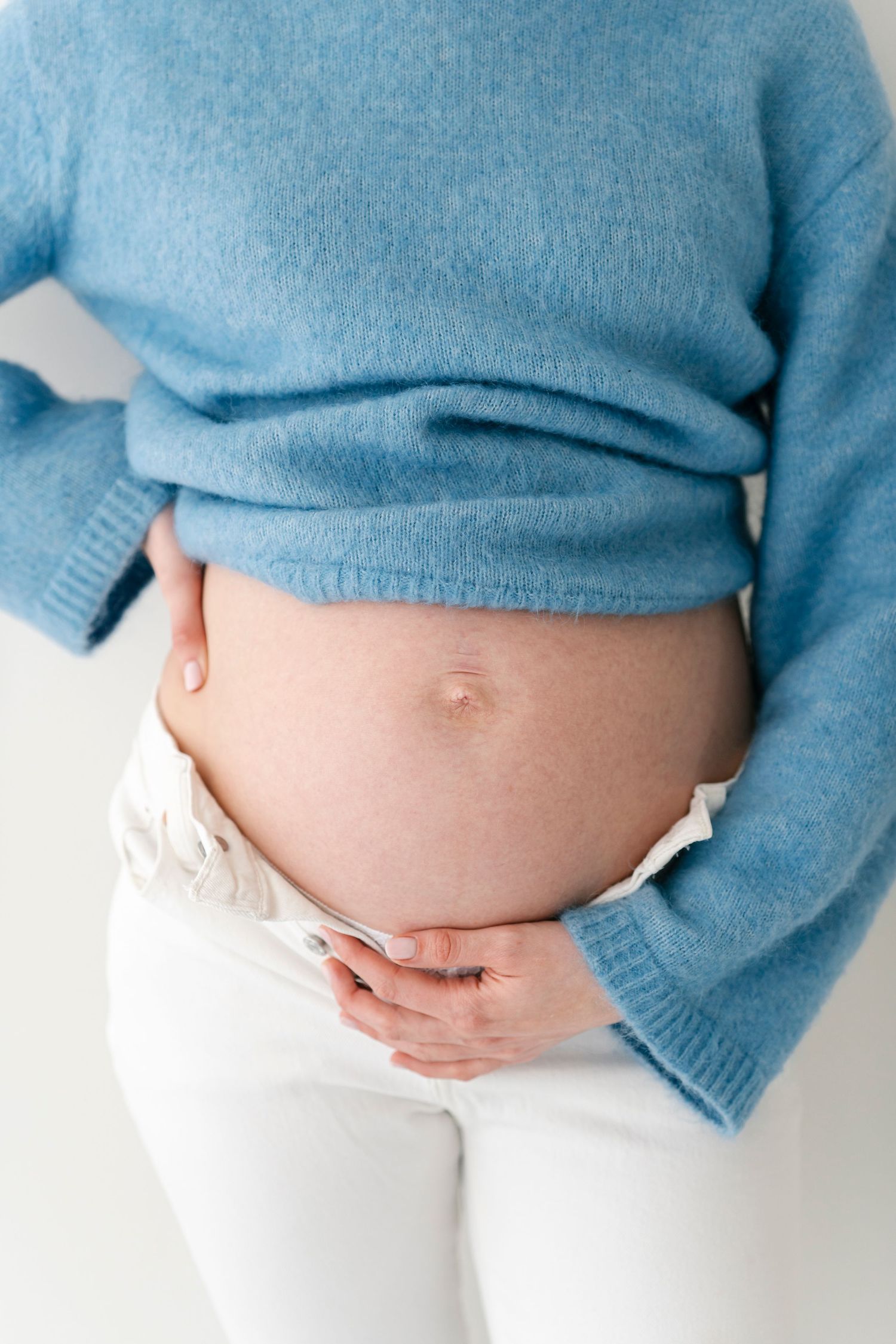 Close-up maternity photos showing pregnant belly with blue sweater and white pants.