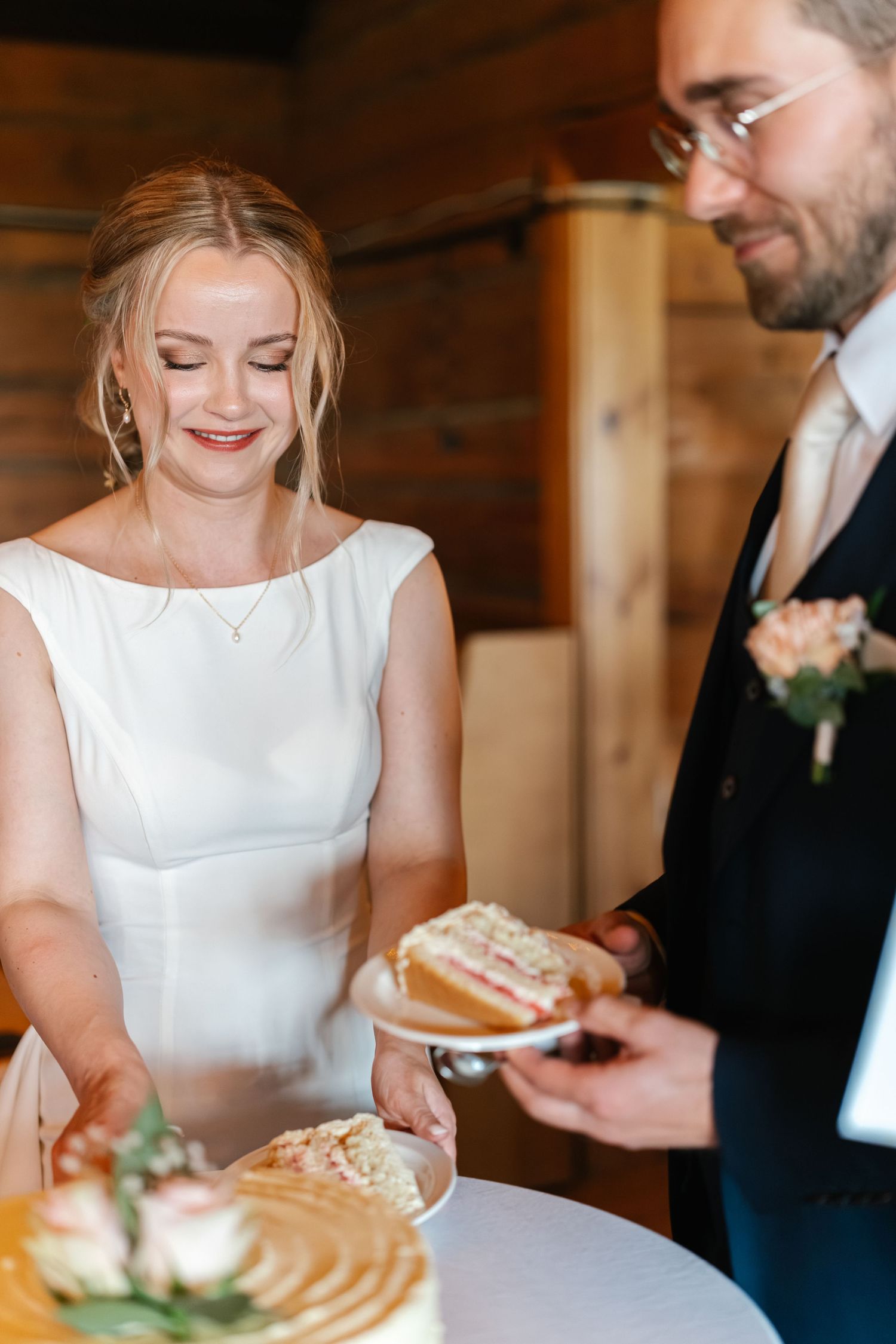 Wedding couple sharing cake at rustic wooden venue during reception.