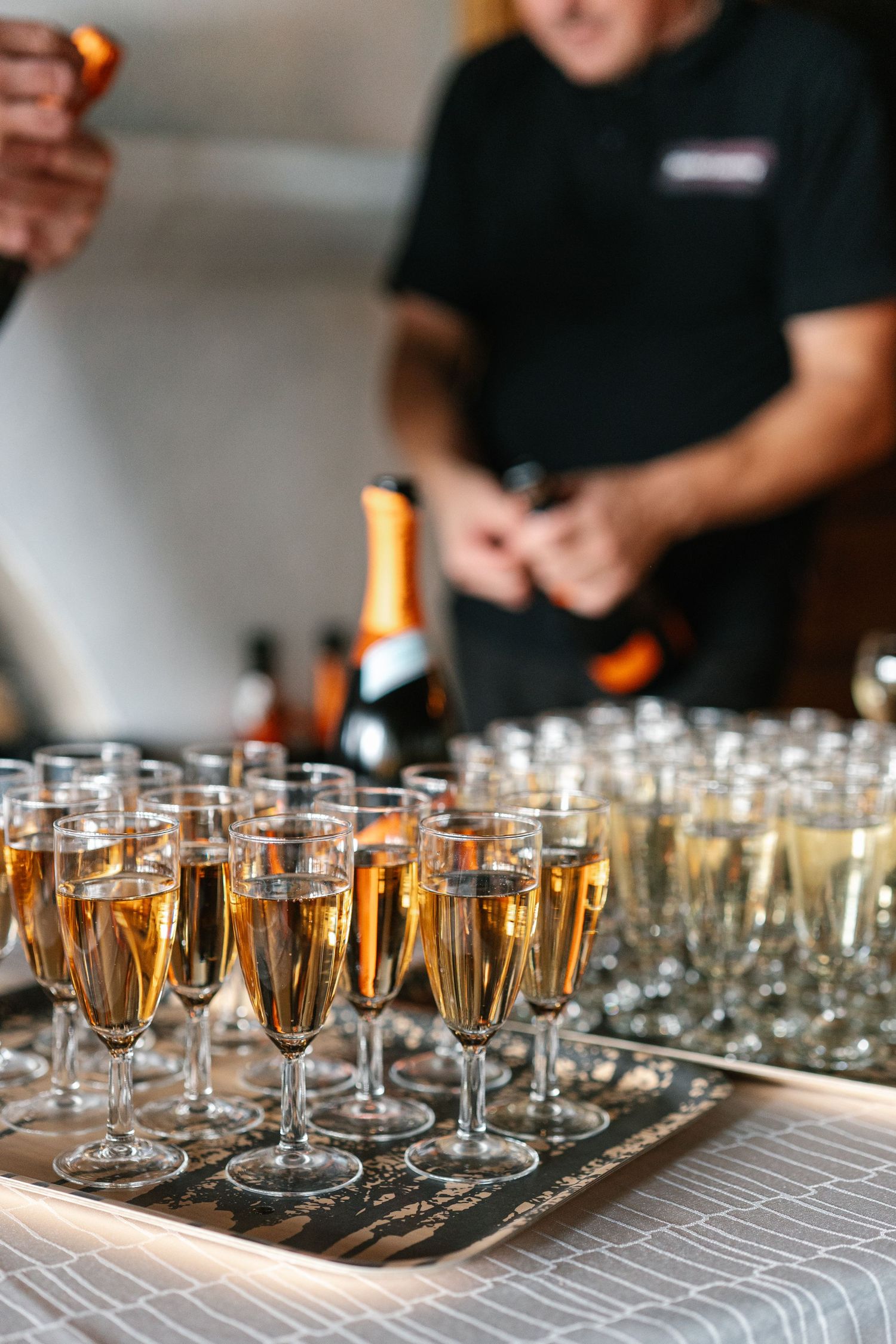 Rows of champagne glasses filled with golden bubbly lined up on a gray tablecloth at an elegant event.