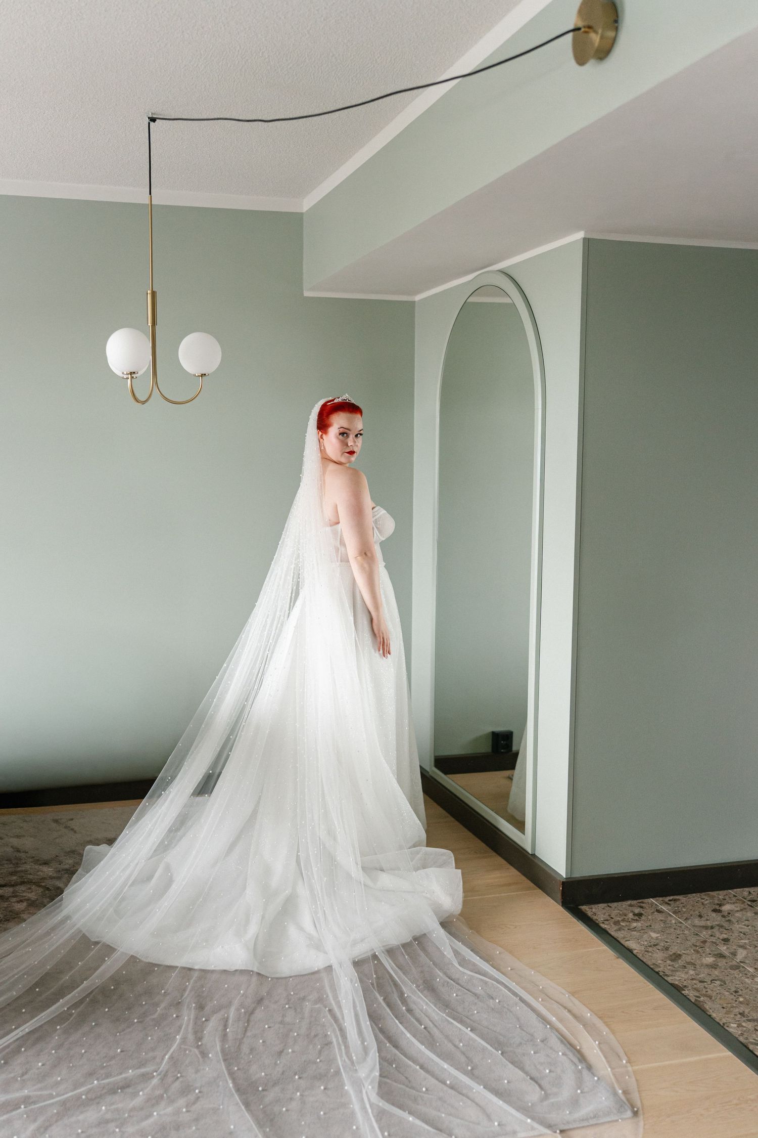 A dramatic wedding dress train spreads across a light-colored floor in an elegant room.