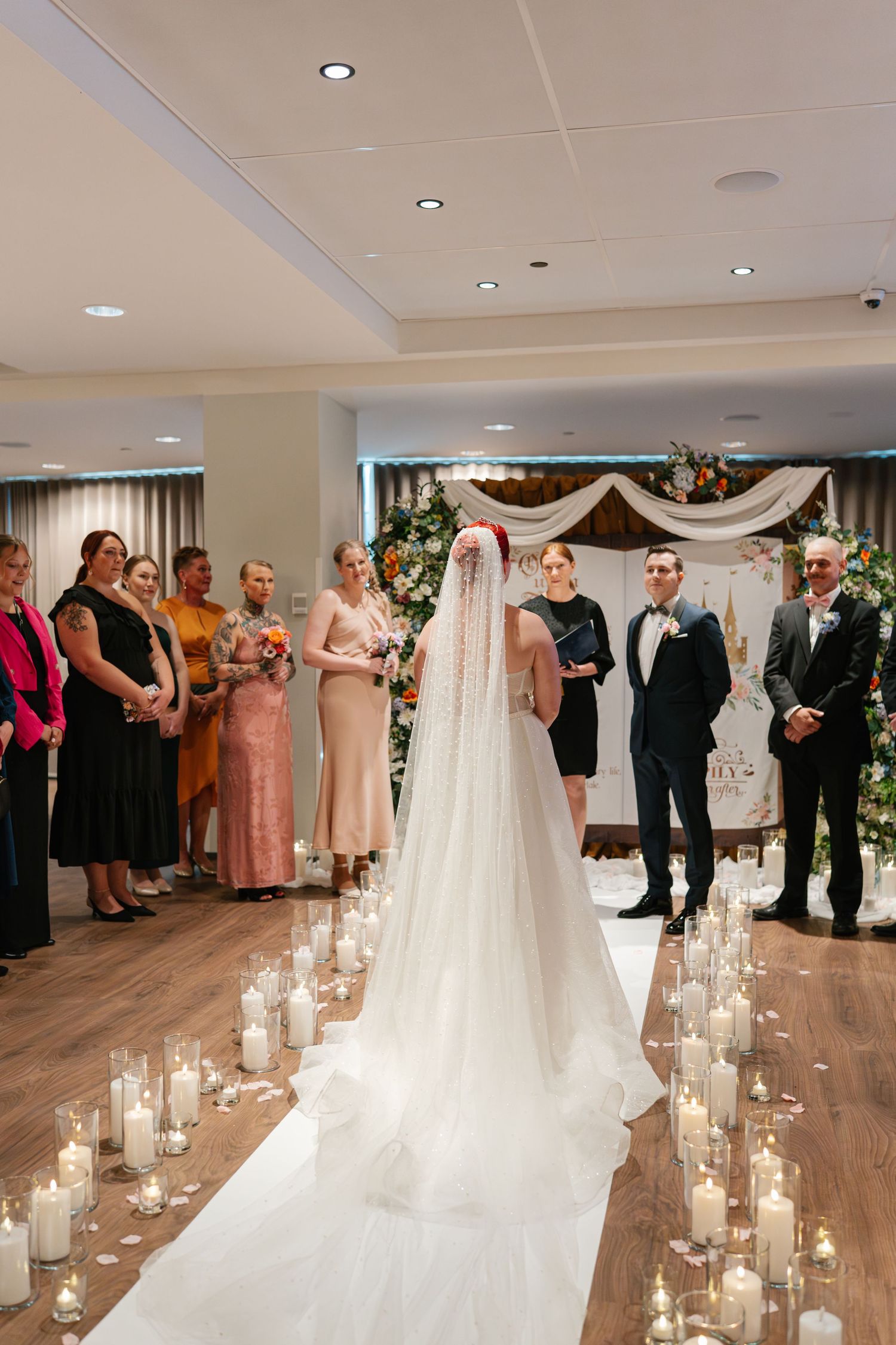 Wedding ceremony aisle lined with glowing candles in glass holders leading to a floral arch.