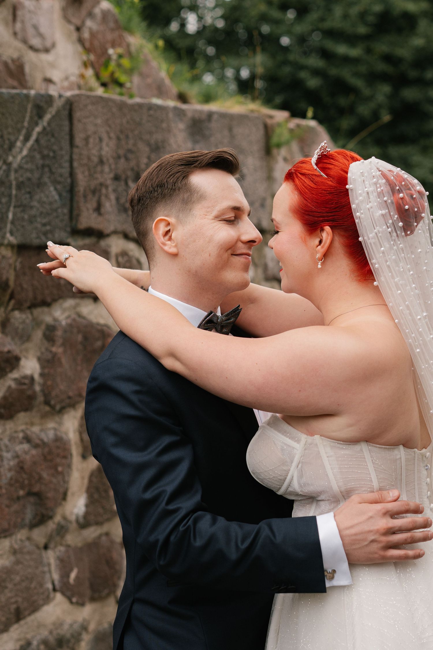 Tender embraces between newlyweds against rustic stone wall background.