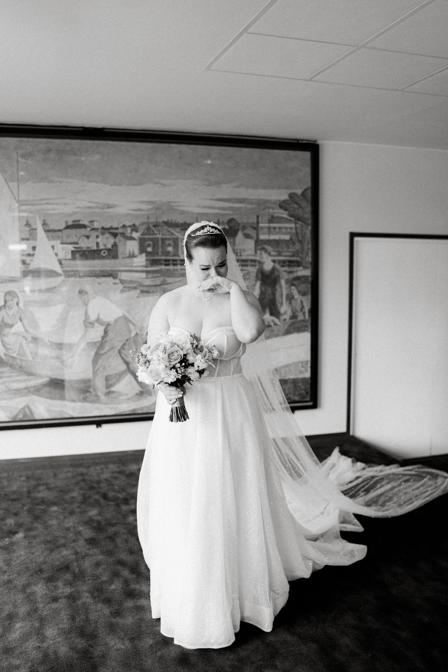 Black and white photo of a flowing wedding dress against artwork in an elegant room.
