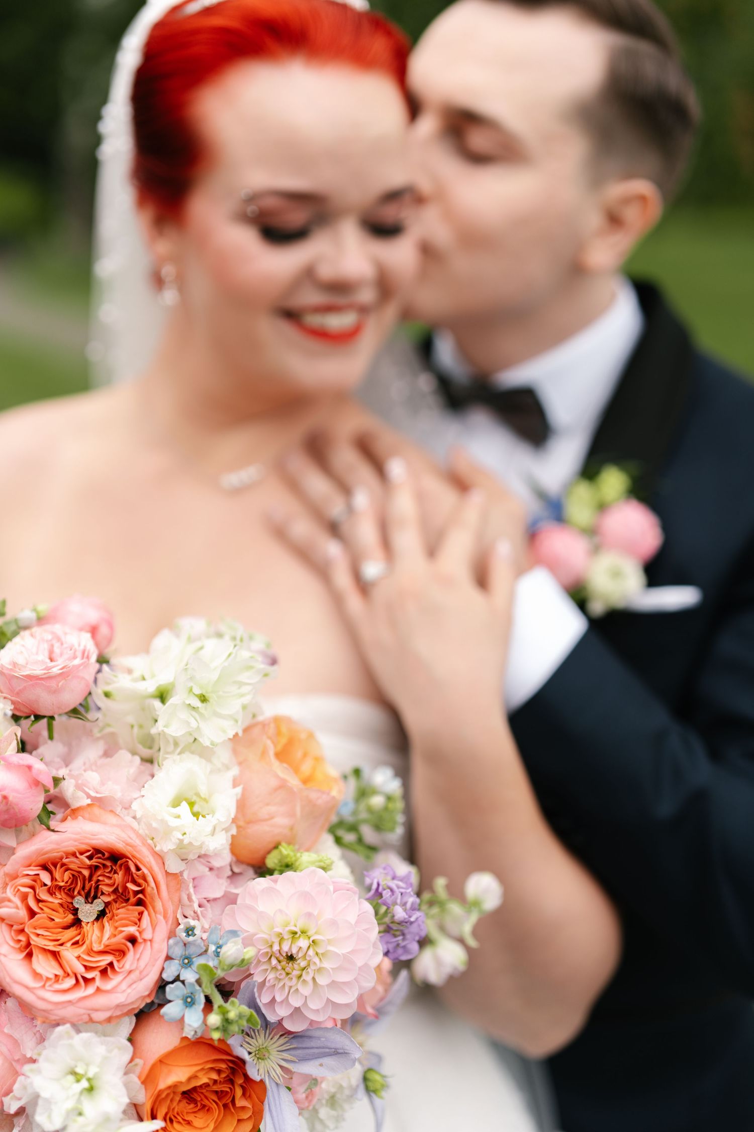 Wedding portrait featuring a beautiful coral and pink floral bouquet with romantic couple in background.