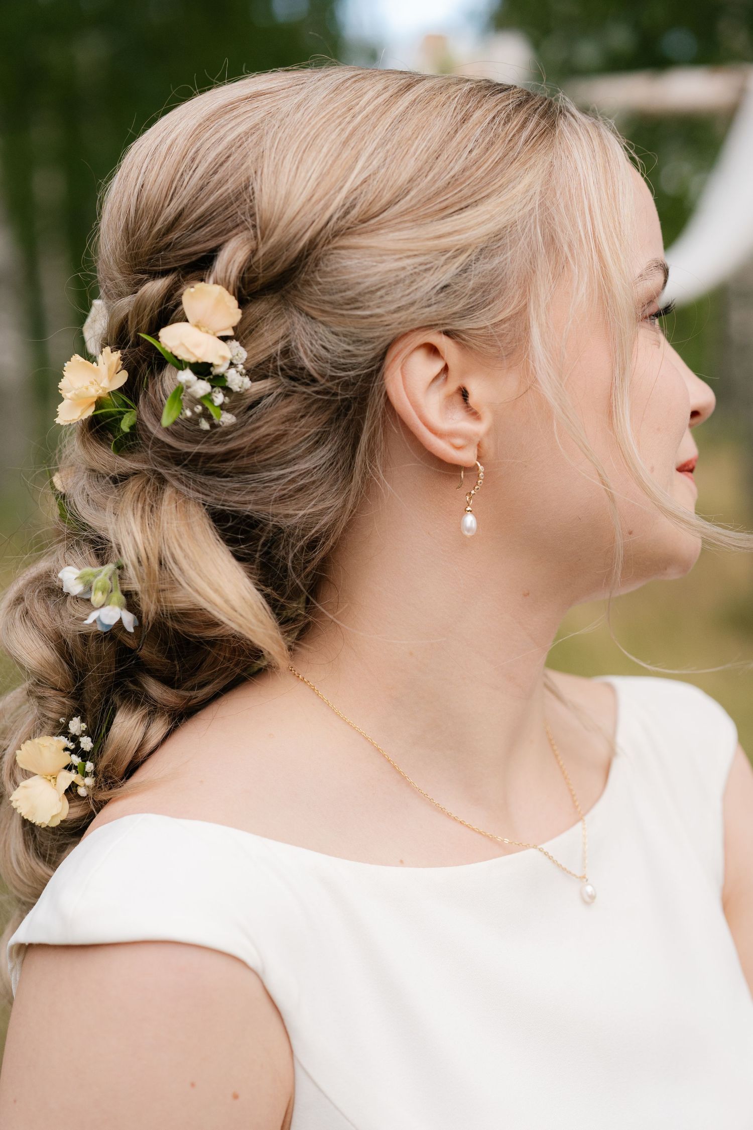 Elegant bridal hairstyle with delicate yellow flowers and pearl earring.