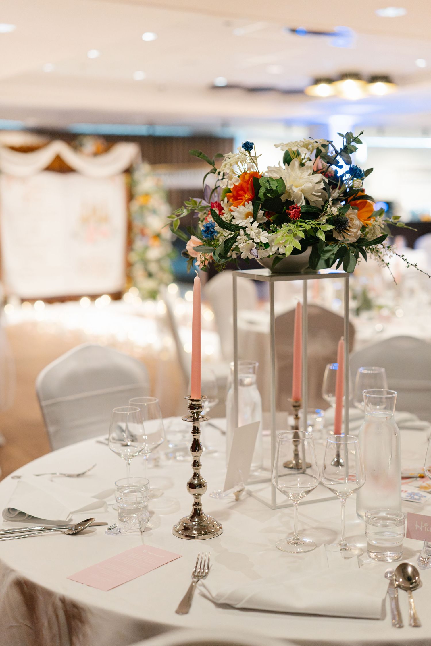 Elegant wedding reception tables set with white linens and floral centerpieces in tall silver candlesticks.