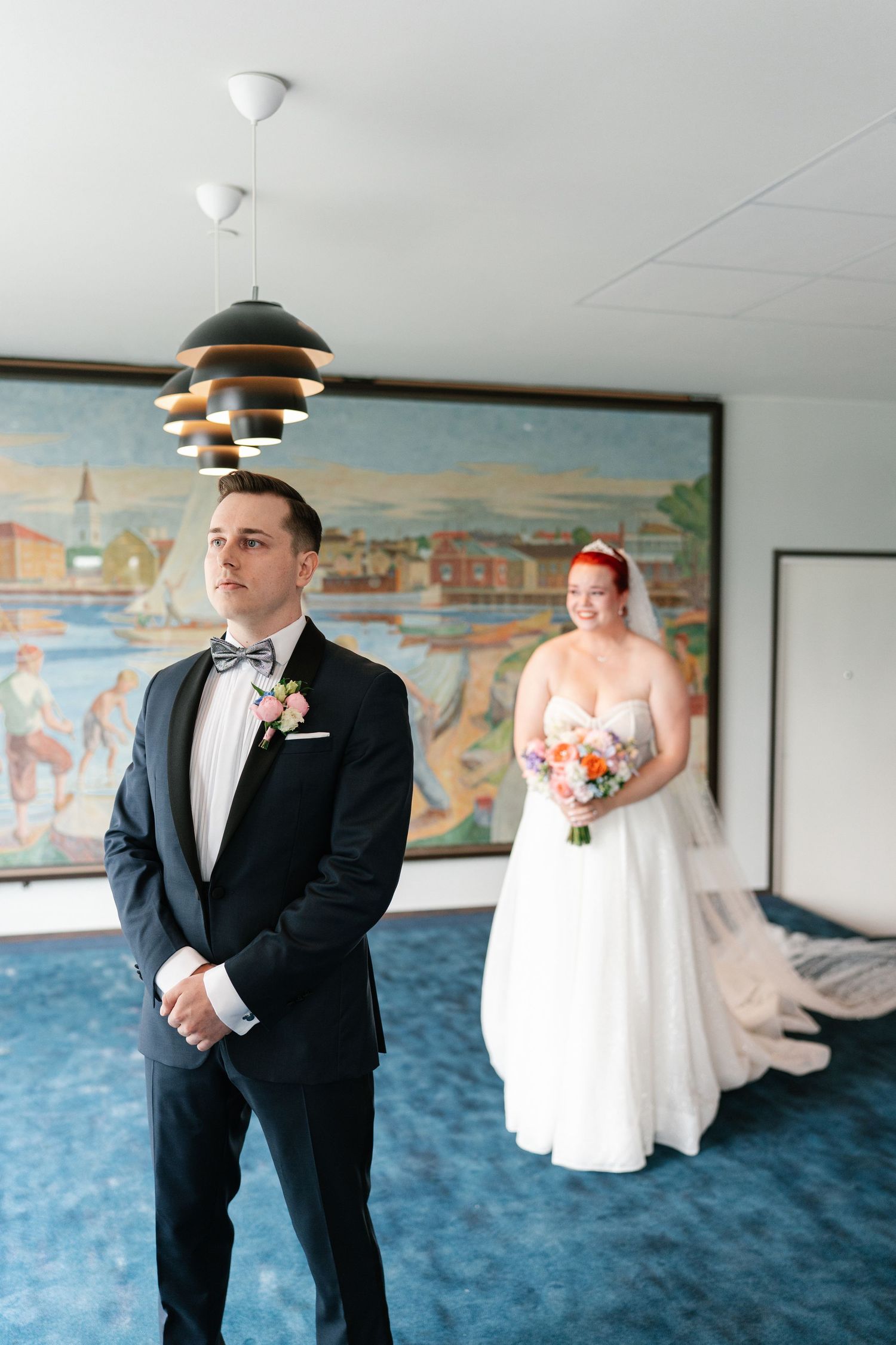 A first look wedding moment captured in a room with blue carpet and coastal artwork.