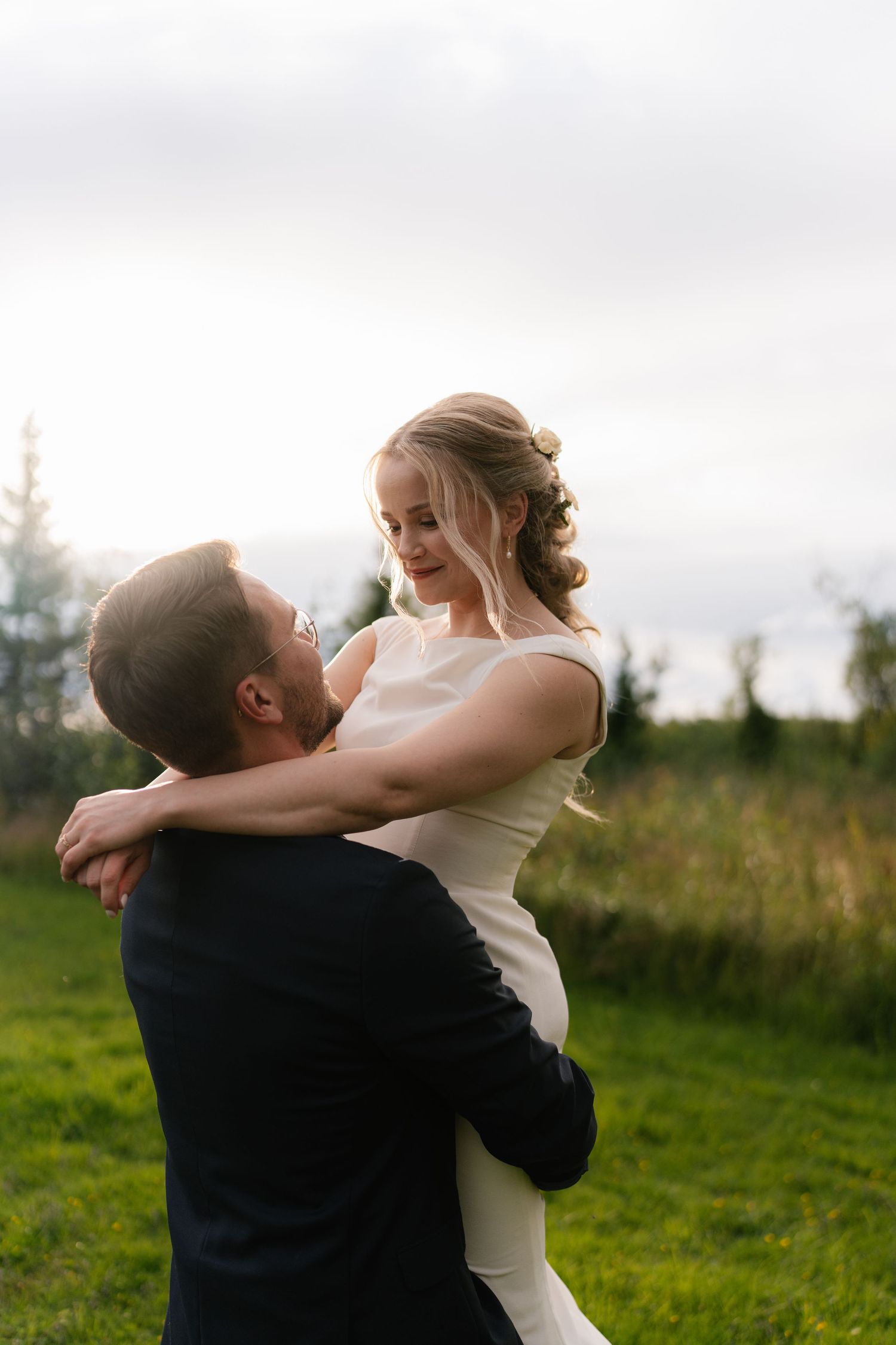 Joyful wedding couple embracing in a sunlit meadow with pine trees.