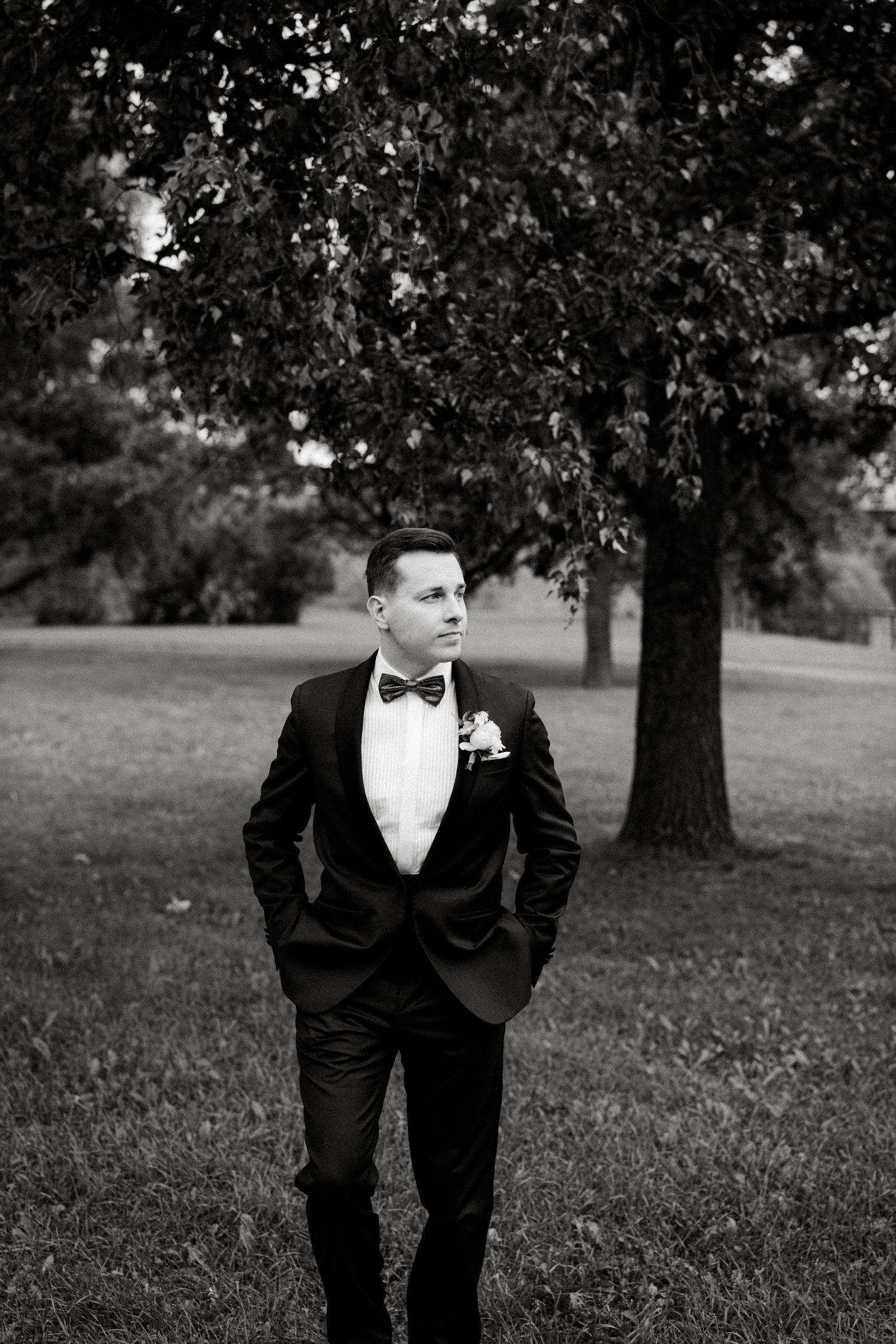 Black and white portrait of a groom in a classic tuxedo and bow tie outdoors.