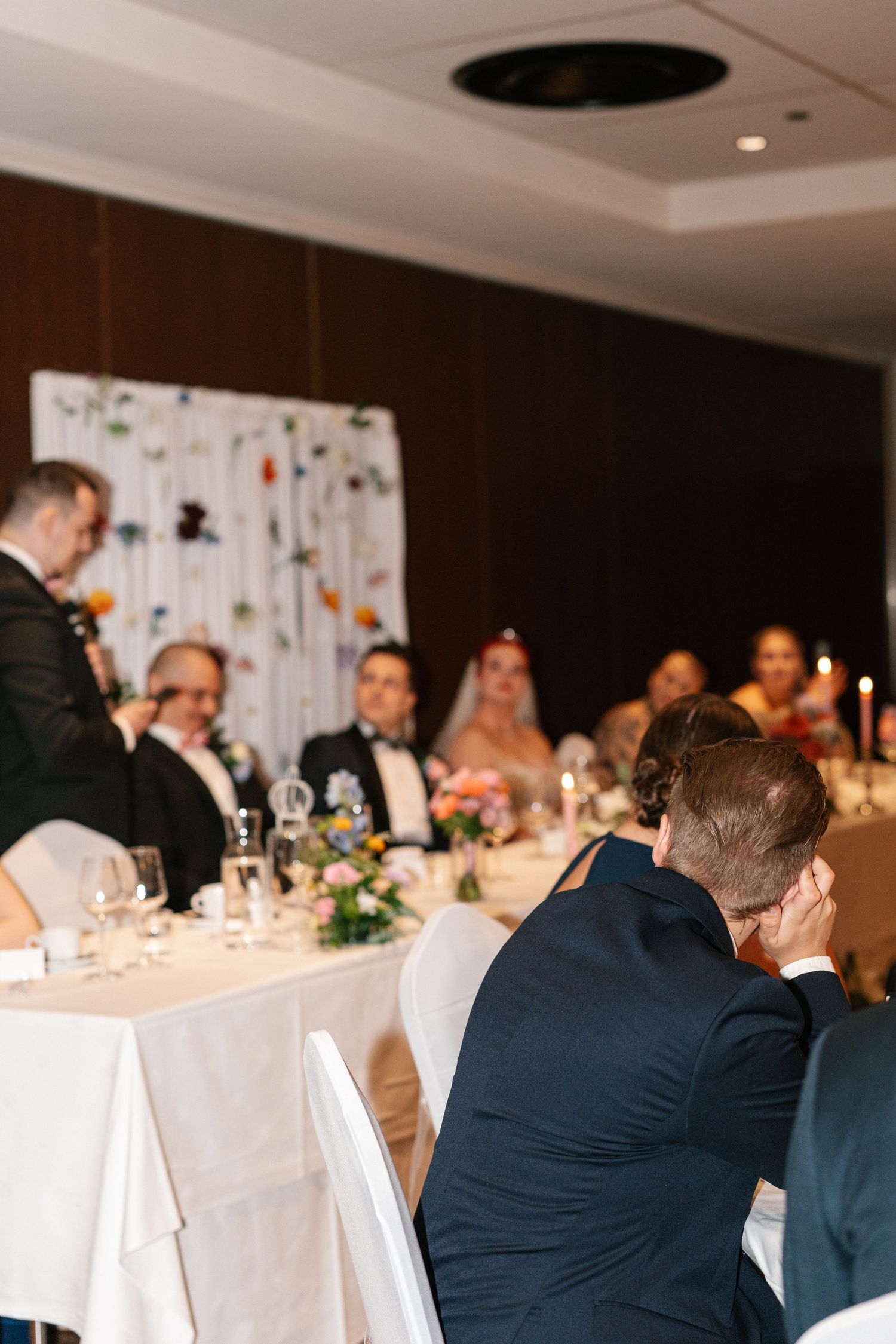 Wedding reception venue with guests seated at tables decorated with white linens and floral arrangements.
