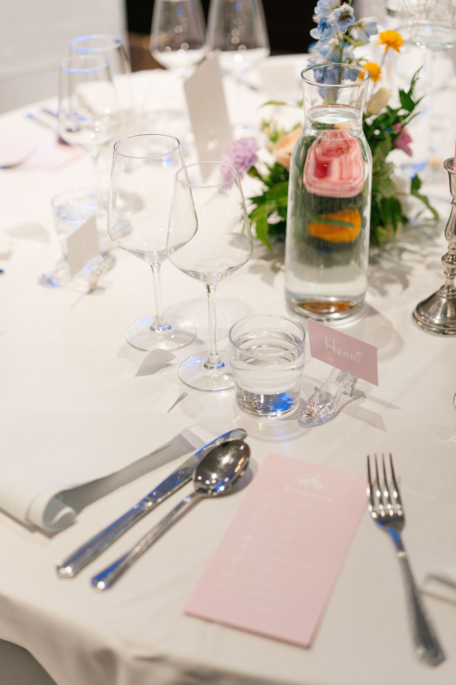 Elegant table settings with wine glasses and pink place cards at a formal reception.