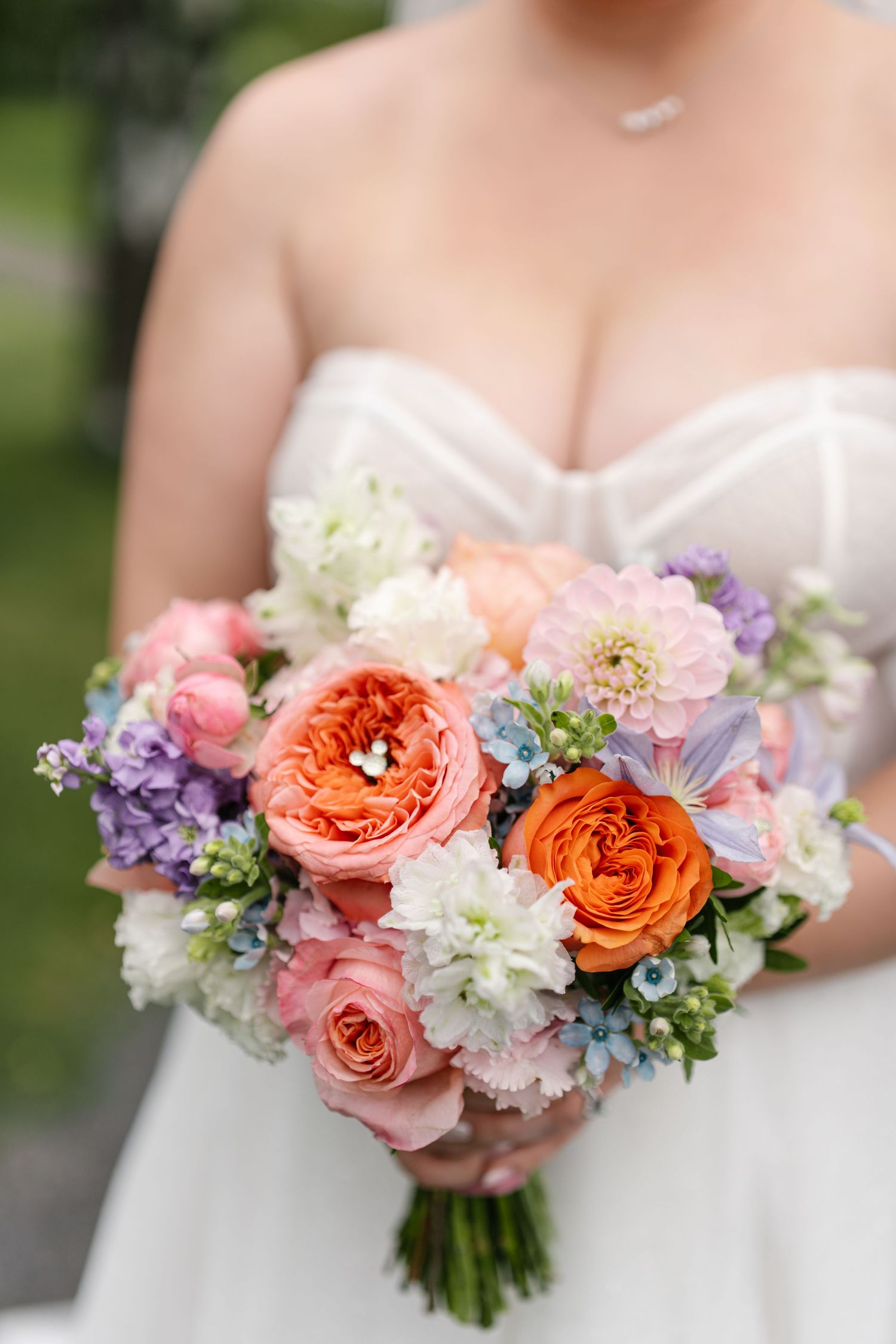 Close-up of vibrant coral and pink bridal bouquet with mixed flowers and greenery.