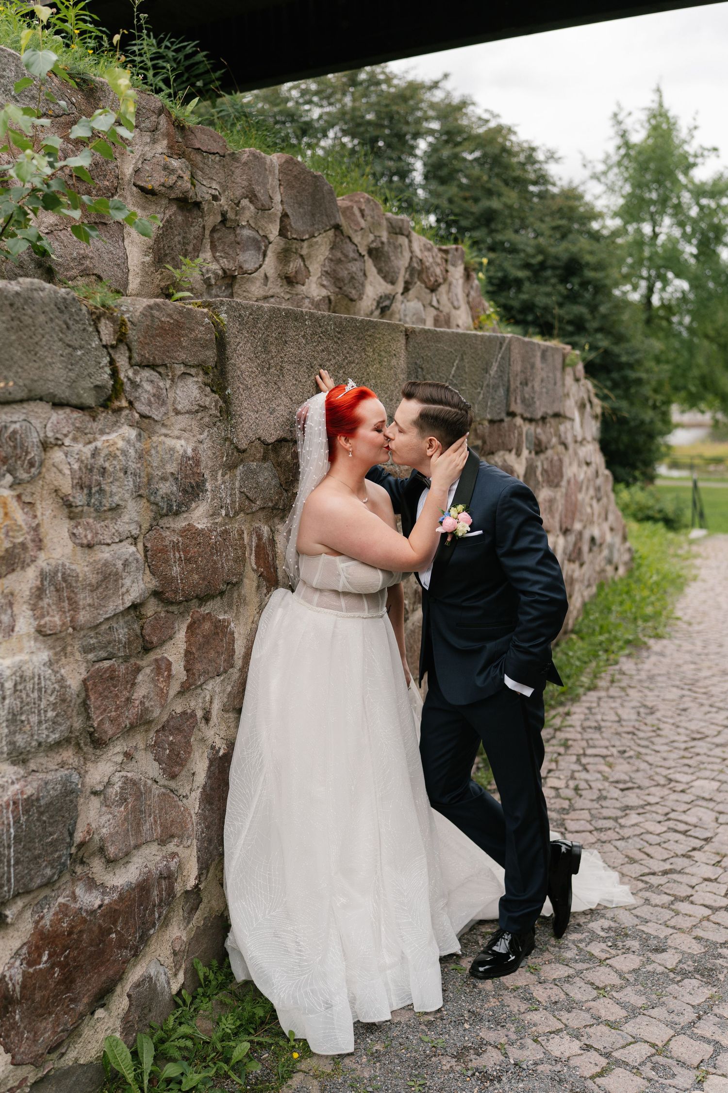 Romantic wedding couple posing against rustic stone wall.