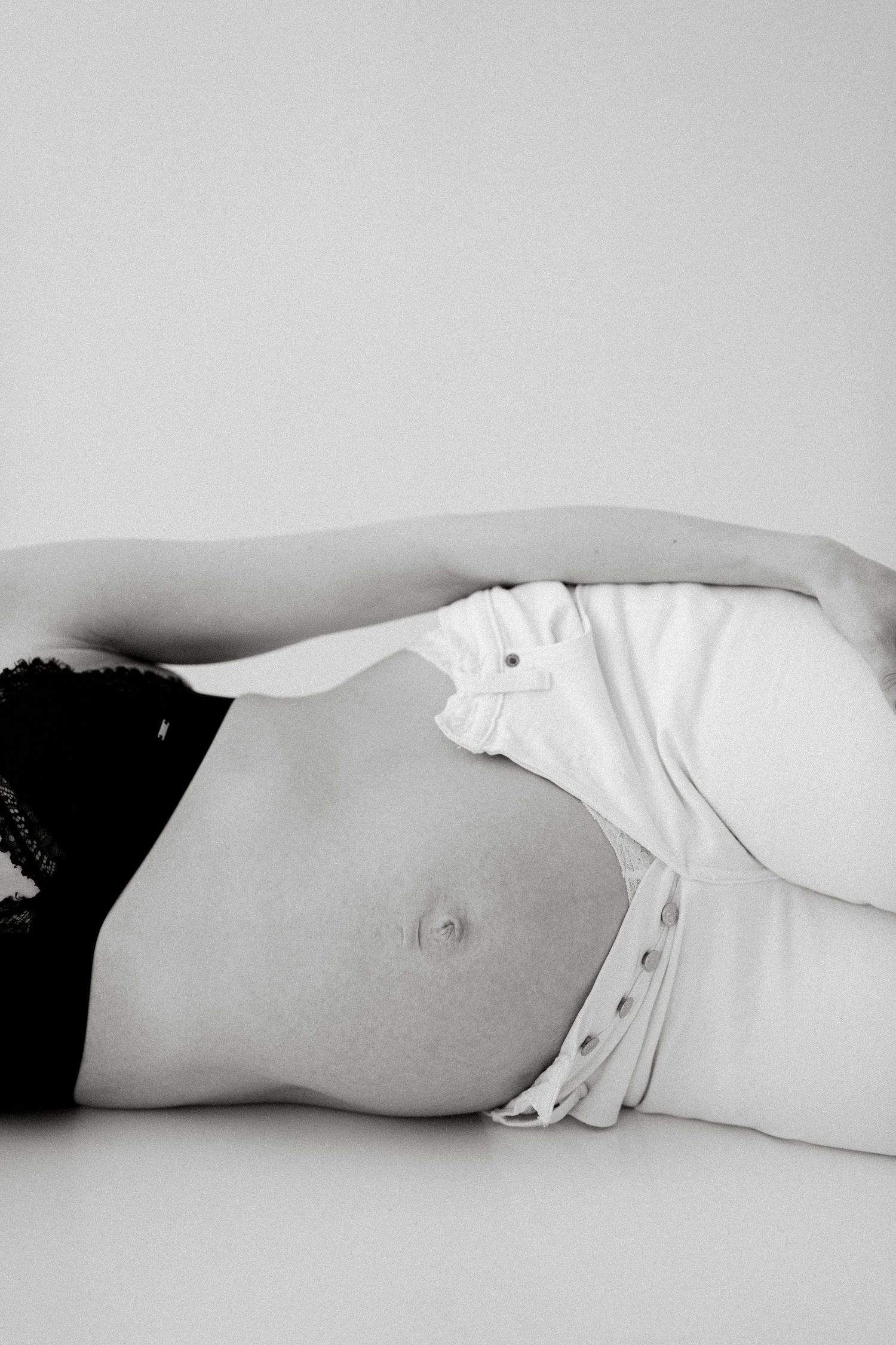 Minimalist black and white maternity photo showing reclining silhouette against light background.