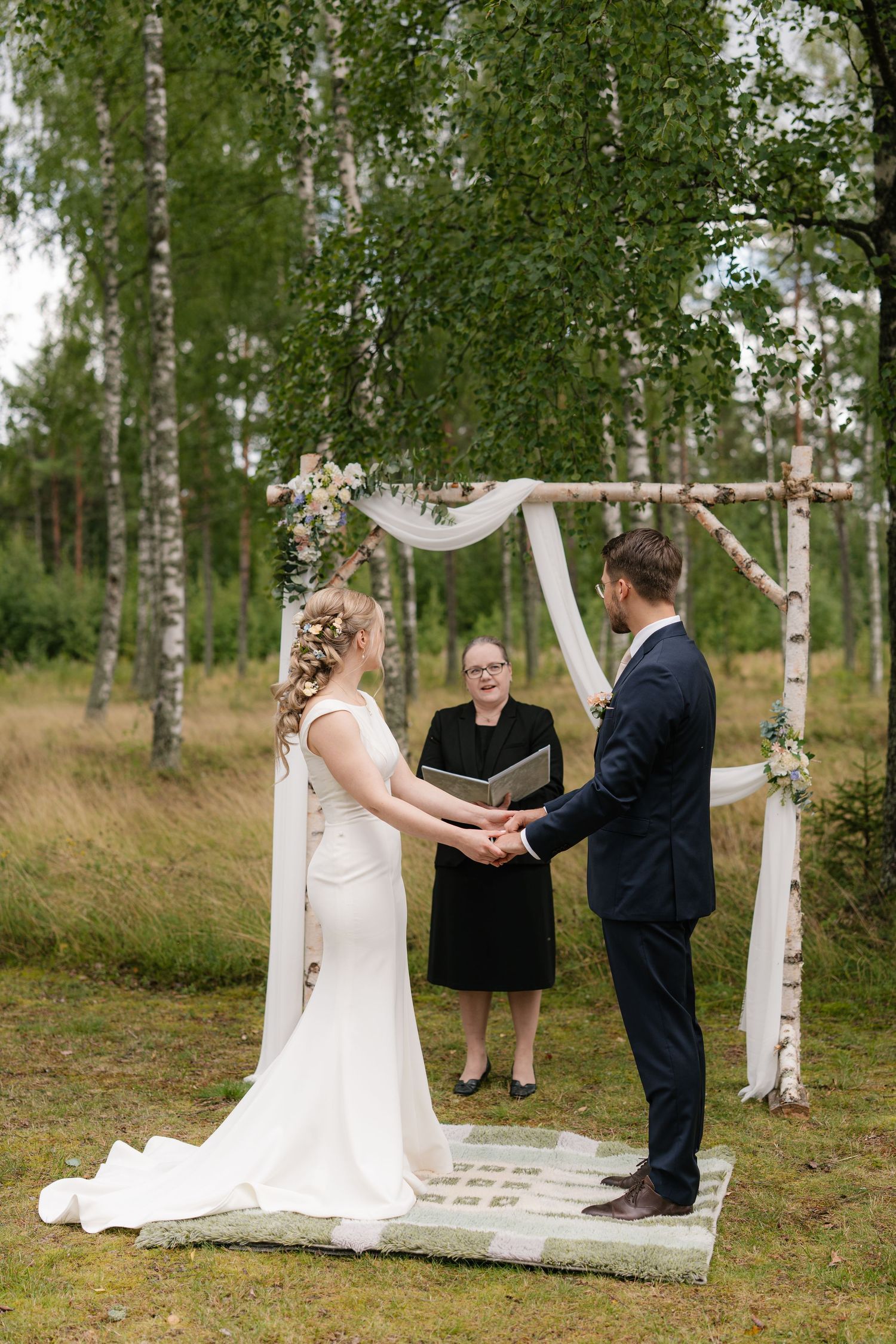 Intimate forest wedding ceremony with white fabric arch and birch trees creating a natural backdrop.