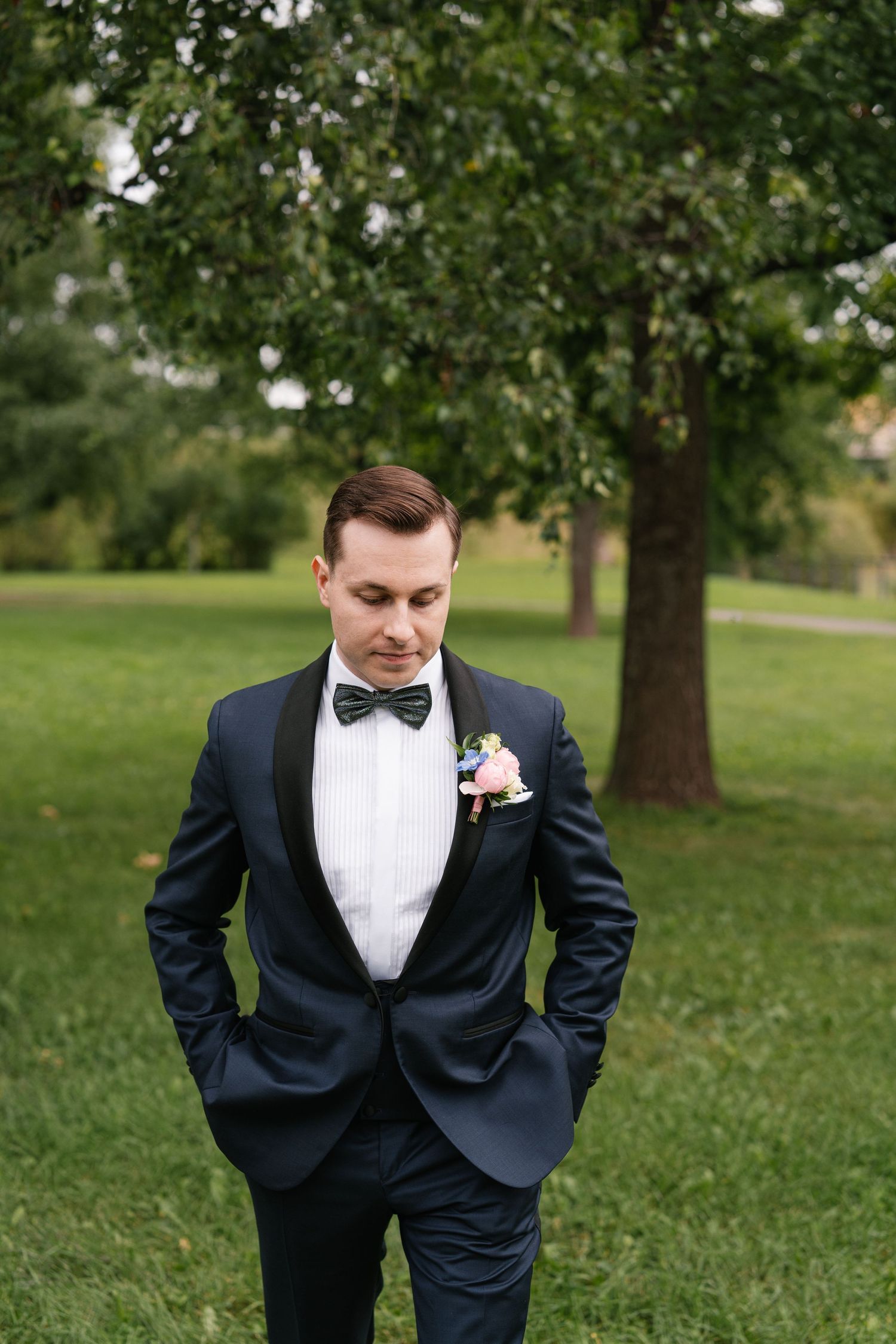 Groom in formal black tuxedo poses in a garden setting.