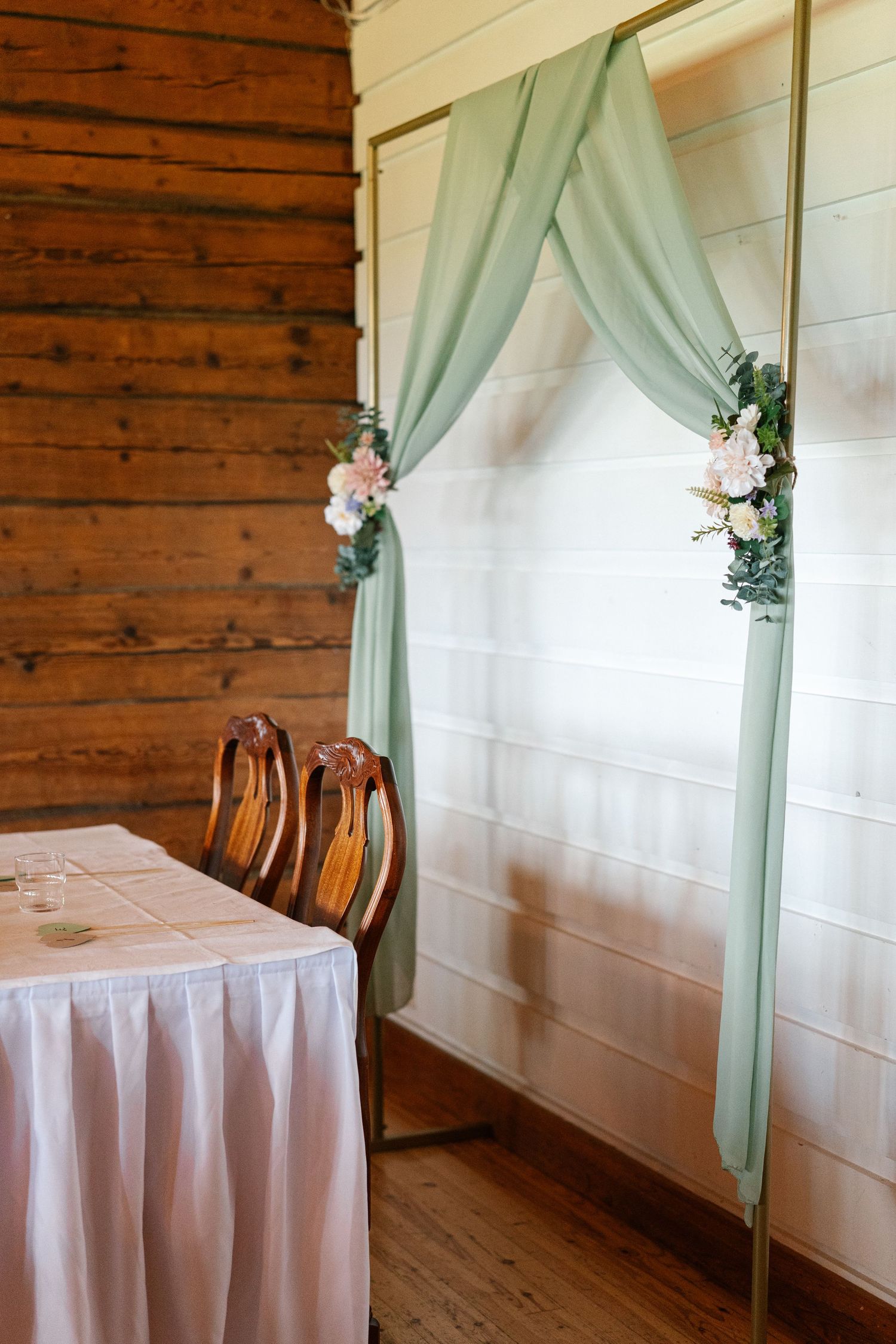 Mint green fabric draped elegantly with floral accents against white walls and wooden panels at a wedding venue.