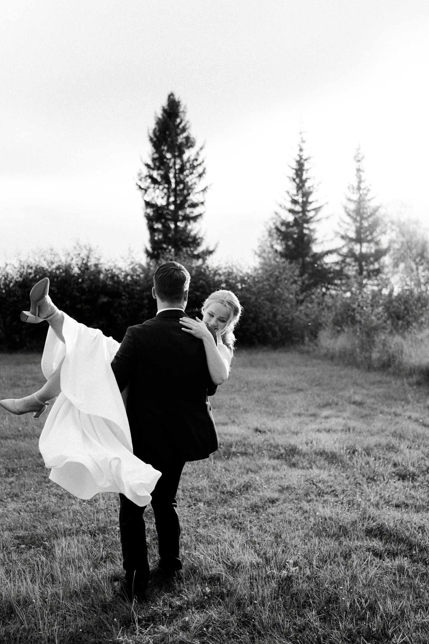 Black and white wedding photos capture a couple's joyful dance and embrace against a natural outdoor backdrop.
