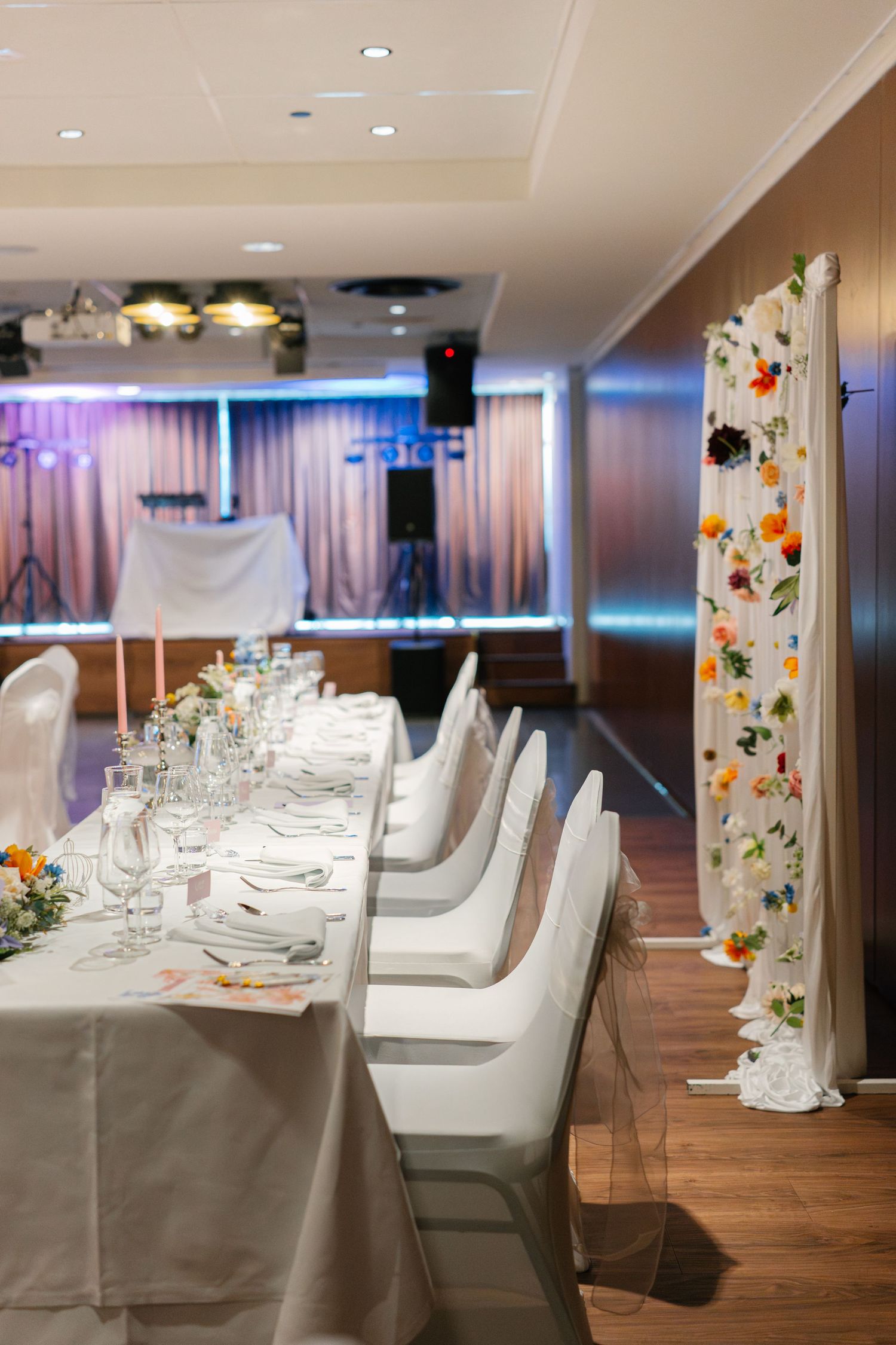 Modern wedding reception hall with white chair covers and hardwood flooring.