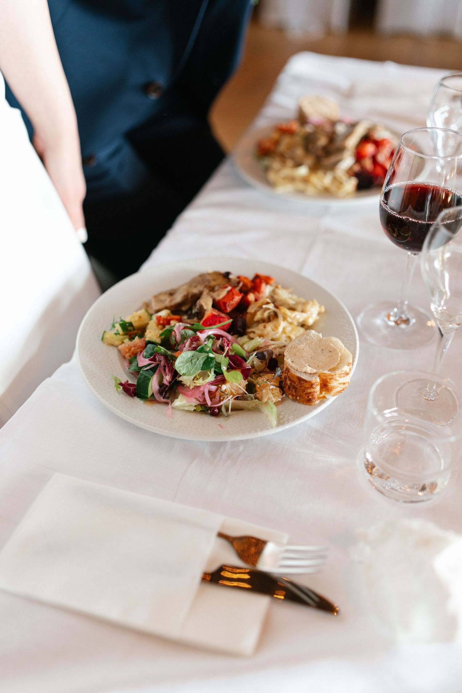 Plated gourmet meals served on white tablecloths with wine glasses.