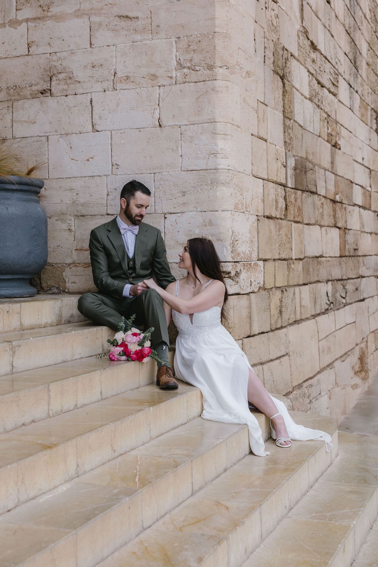 A couple shares a quiet moment on historic stone steps in Palma de Mallorca, framed by a warm limestone wall and soft Mediterranean light.
