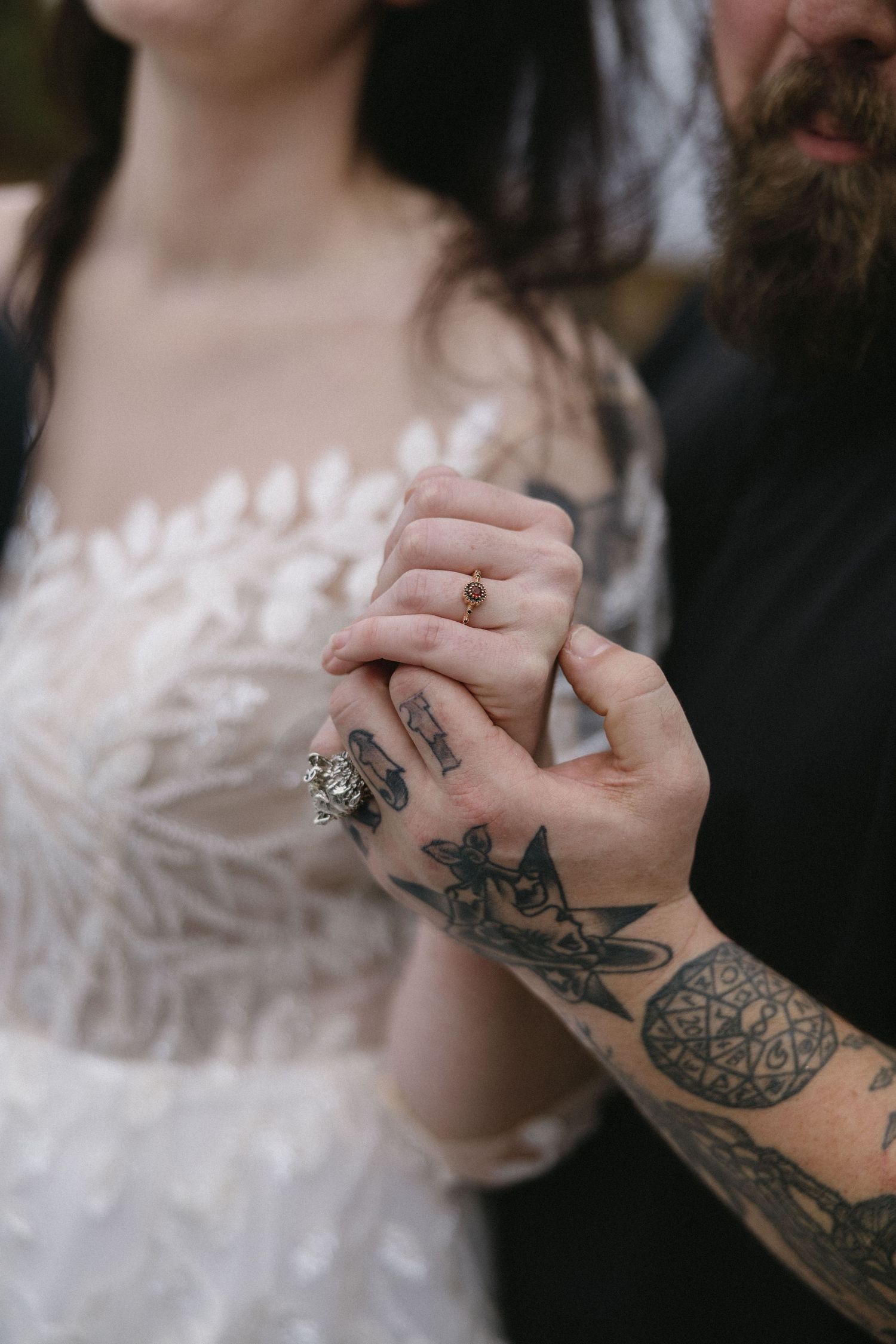 Tattooed hands intertwined, wedding rings gleaming against a white lace dress - love captured in the finest details.