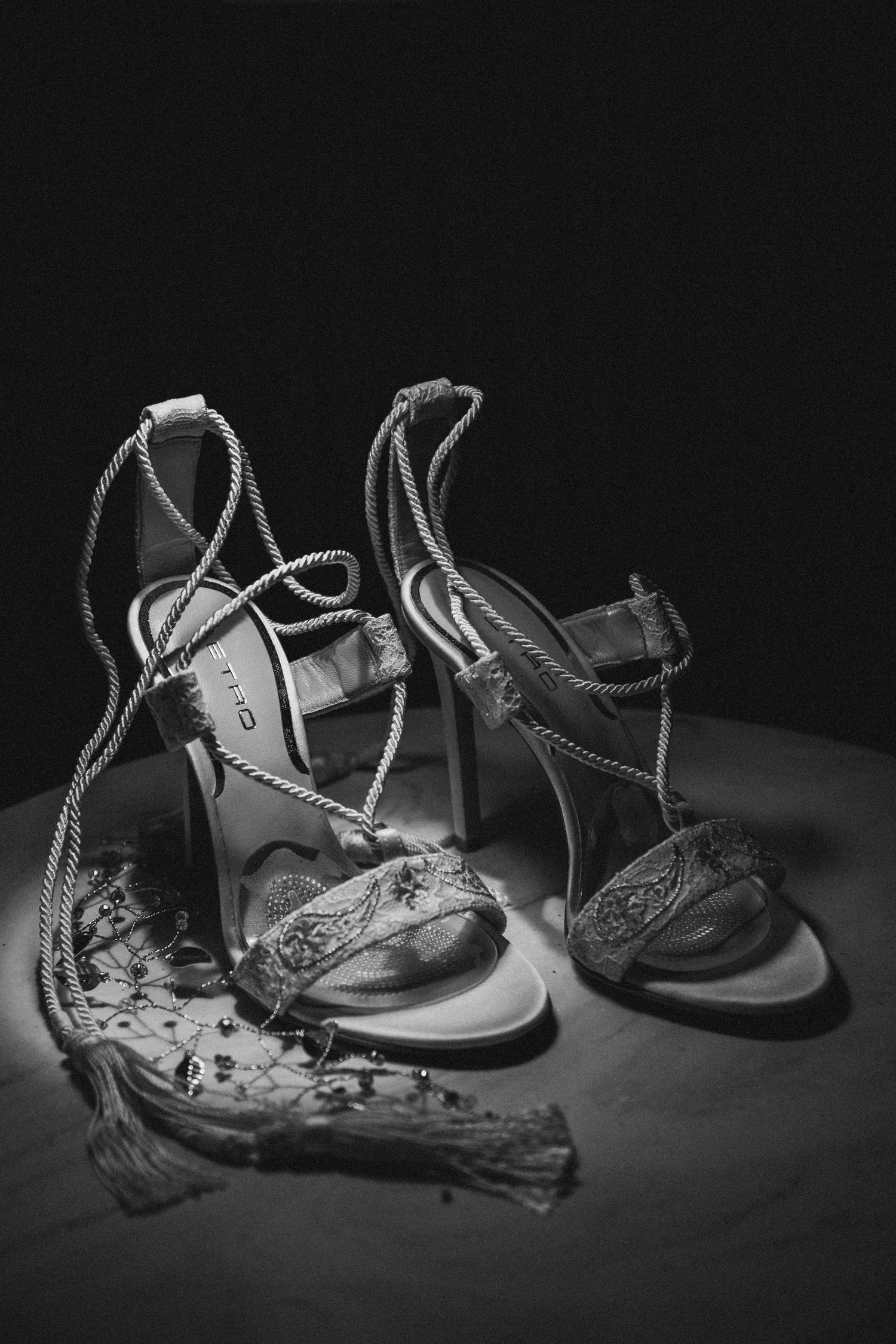 Elegant strappy wedding shoes captured in black and white, their delicate details highlighted against a moody dark backdrop.