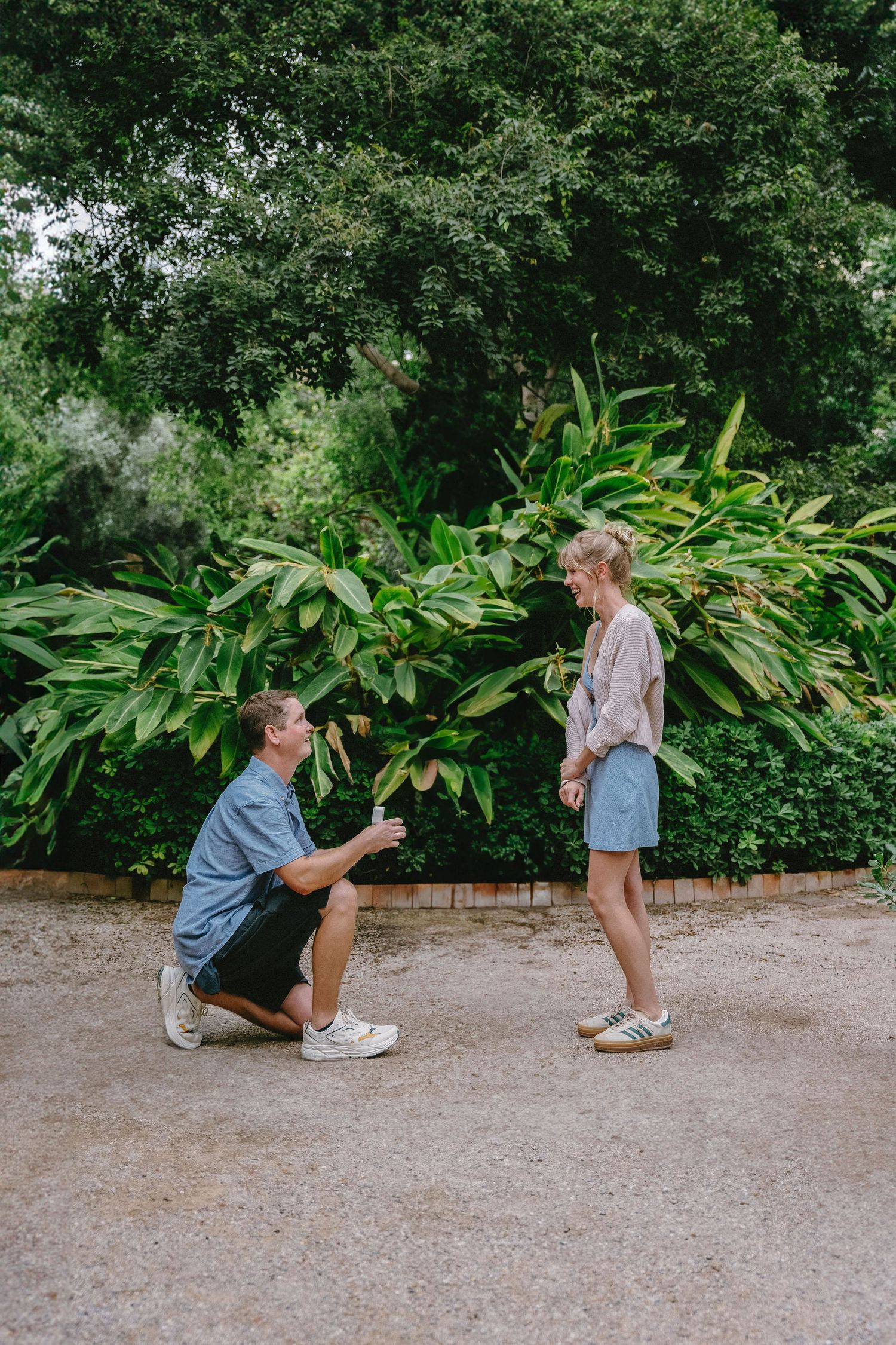 Surprise garden proposal with groom kneeling in lush greenery, surrounded by tropical plants - intimate engagement photography in Spain.