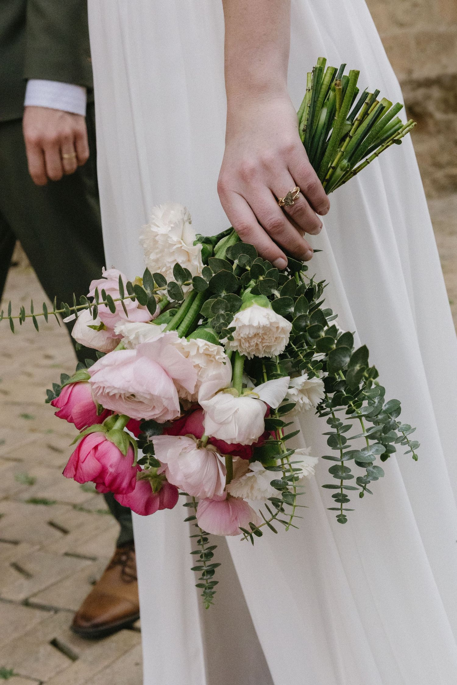 A bride holds a delicate bouquet of blush and white roses, her flowing gown trailing against the rustic stone pathway.