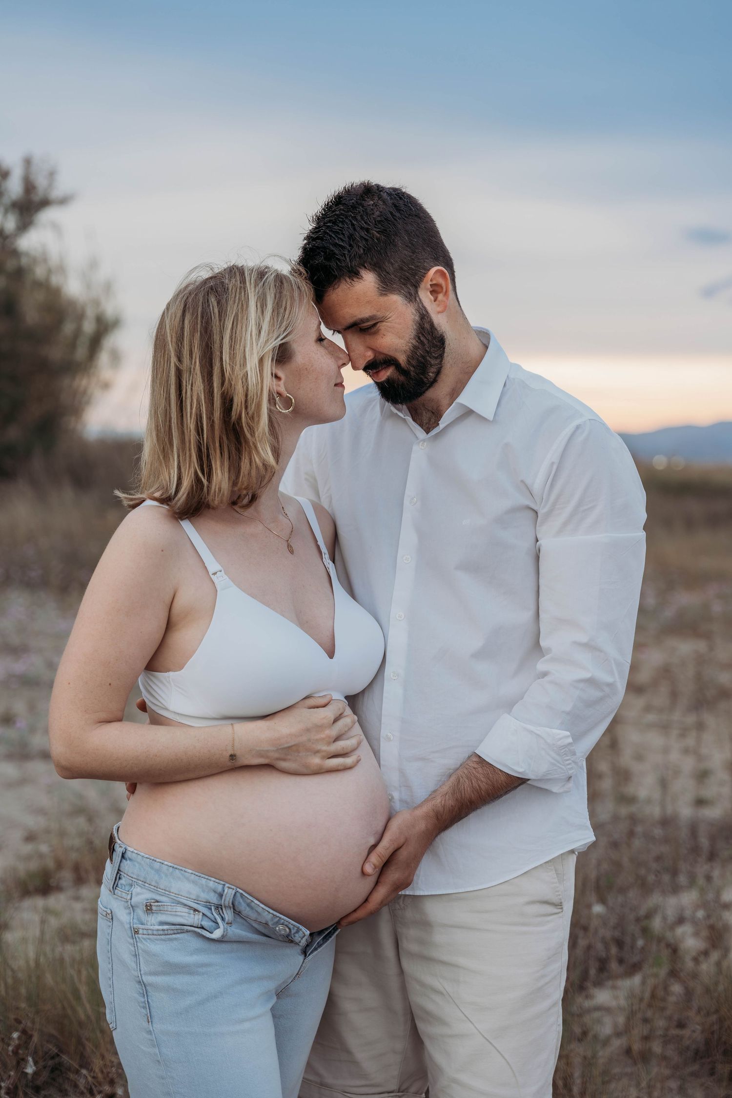 Outdoor maternity portrait at sunset, featuring a couple embracing in a natural setting.