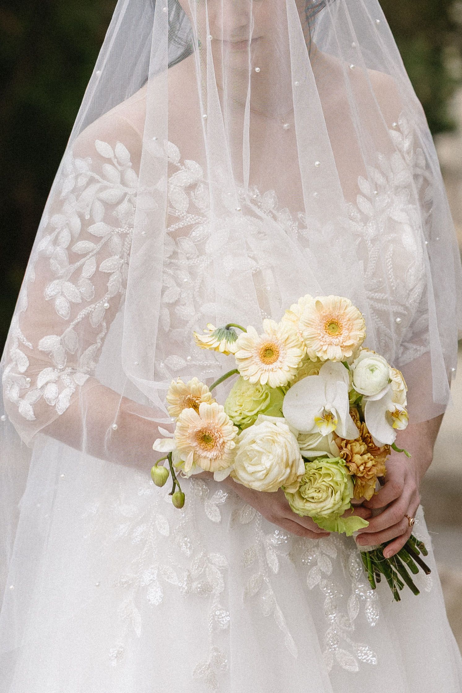 A delicate bridal bouquet of white and peach flowers rests against an embroidered veil, capturing the essence of elegance and romance.