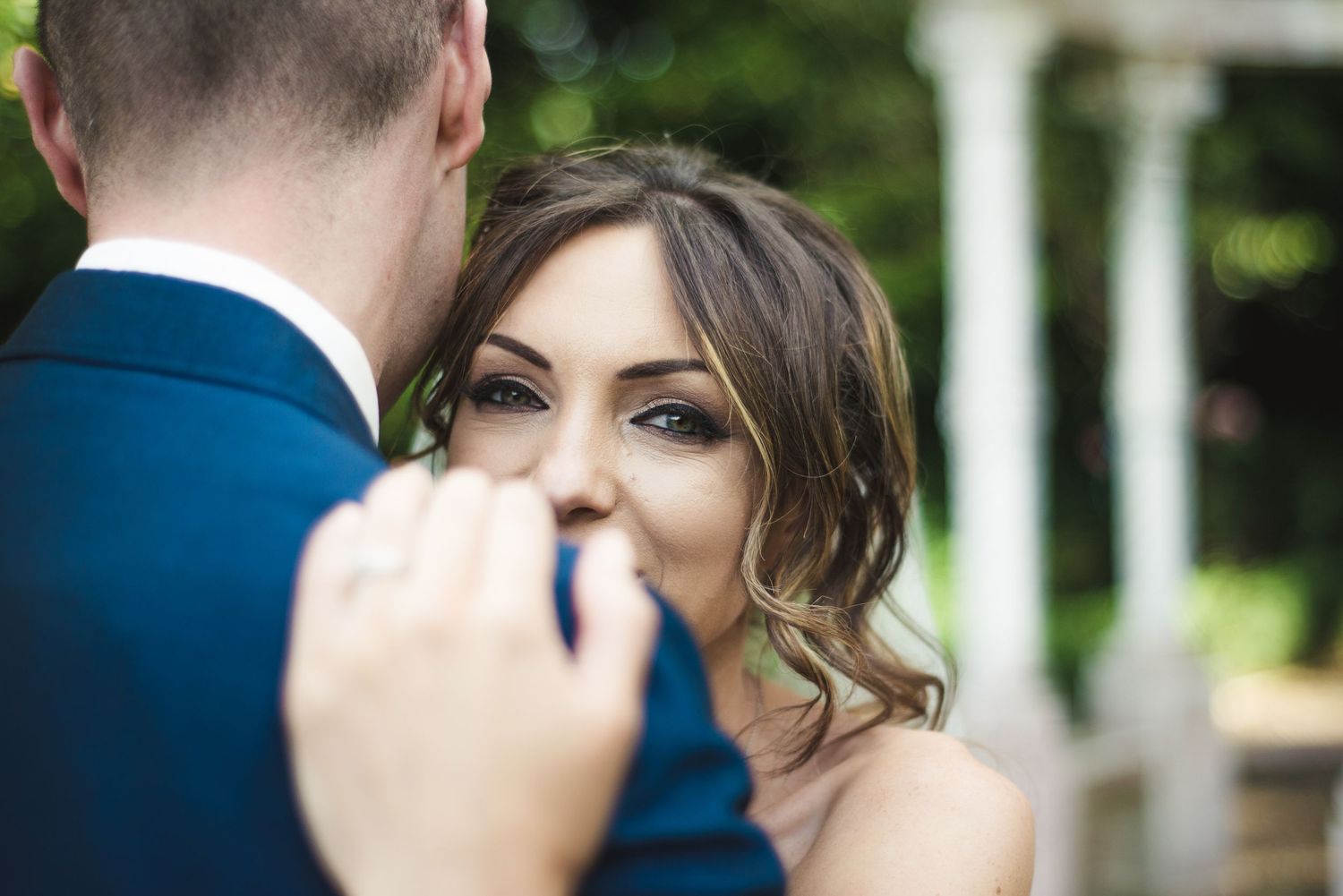 A bride gazes lovingly at her groom in a blue suit during an outdoor wedding ceremony.