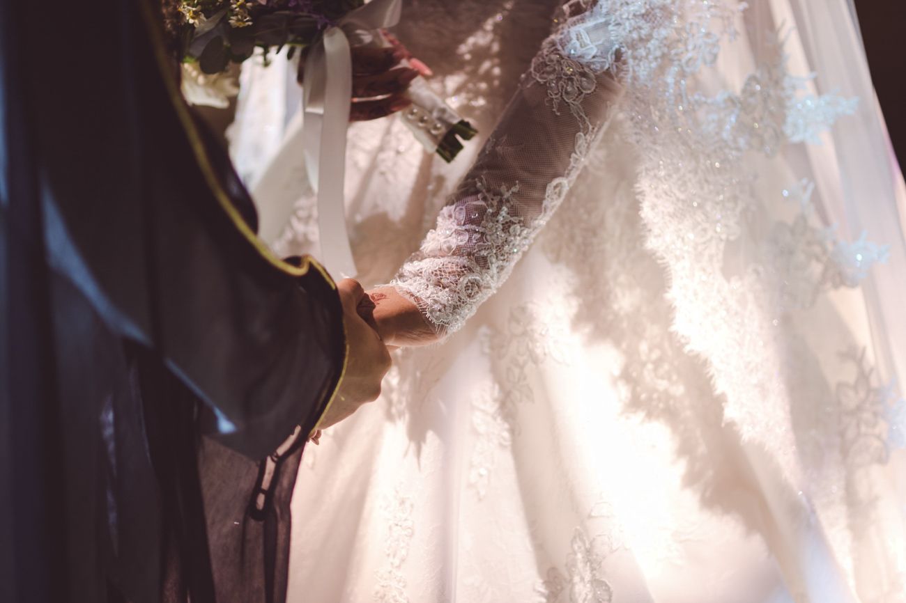 Bride in lace wedding gown holding hands with groom during wedding ceremony.