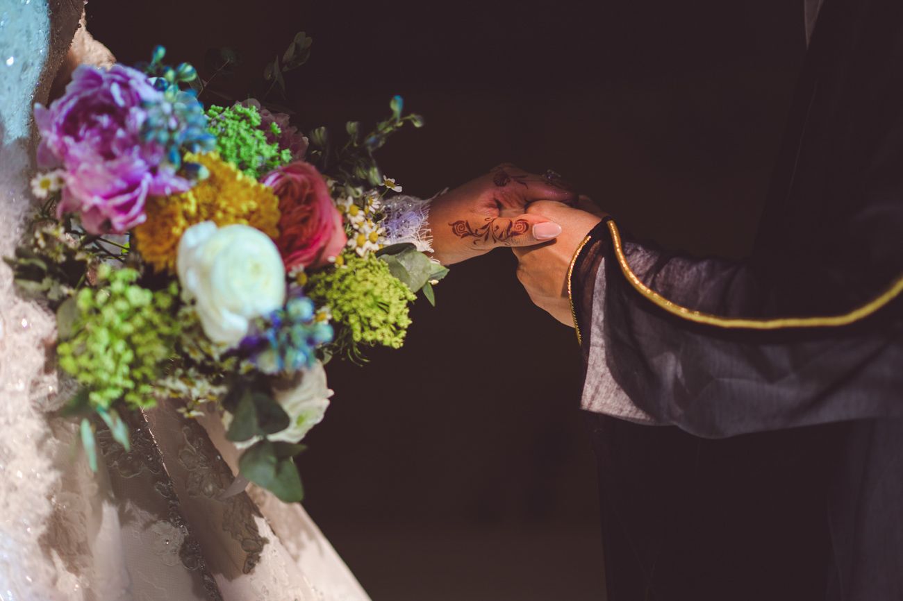Bride and groom exchanging rings with a colorful wedding bouquet featuring purple, pink, and green flowers.