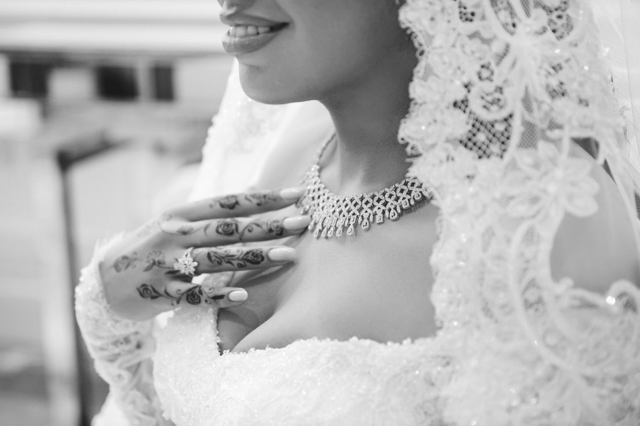 Black and white photo of a bride in lace dress with henna hands, pearl necklace, and veil.