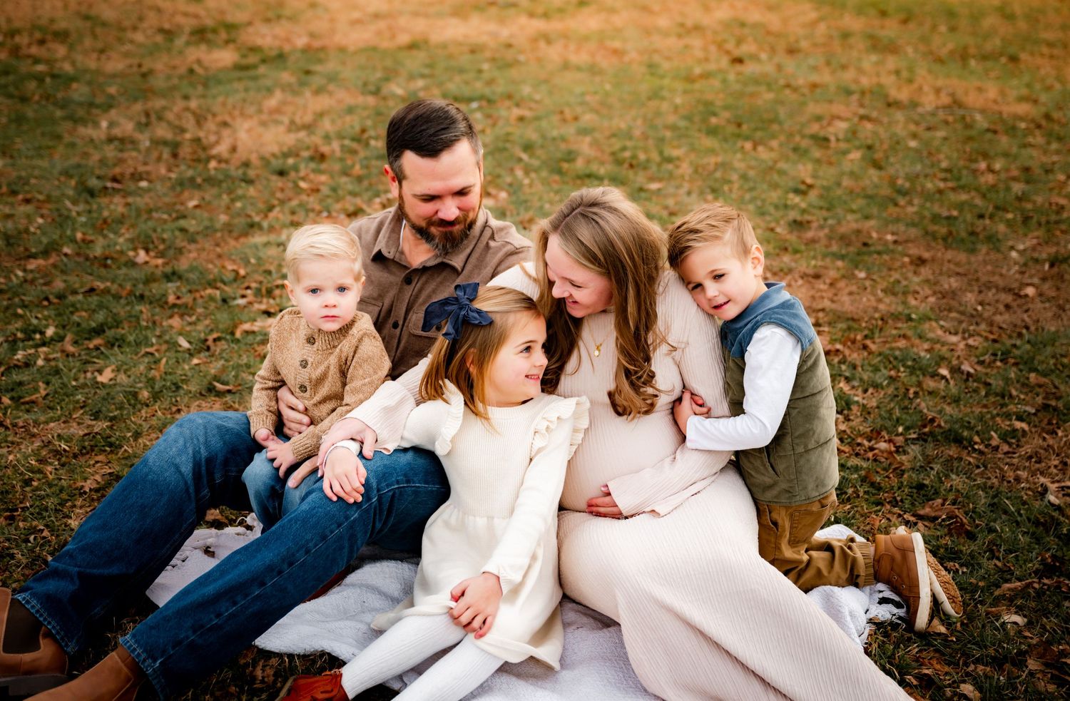 Family enjoying a playful moment together on autumn grass in matching casual outfits.