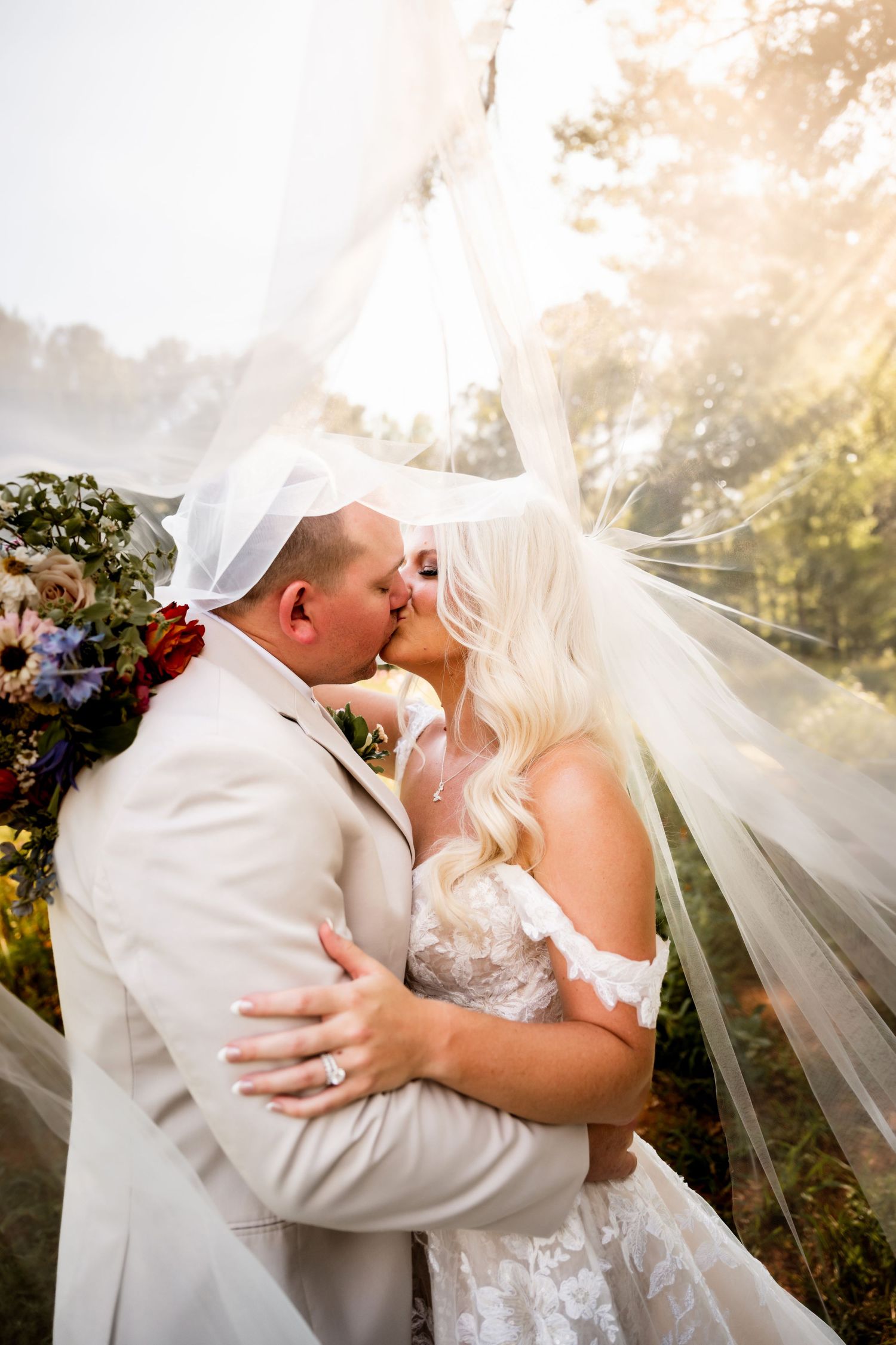 Romantic wedding moment with flowing veil in golden sunlight.