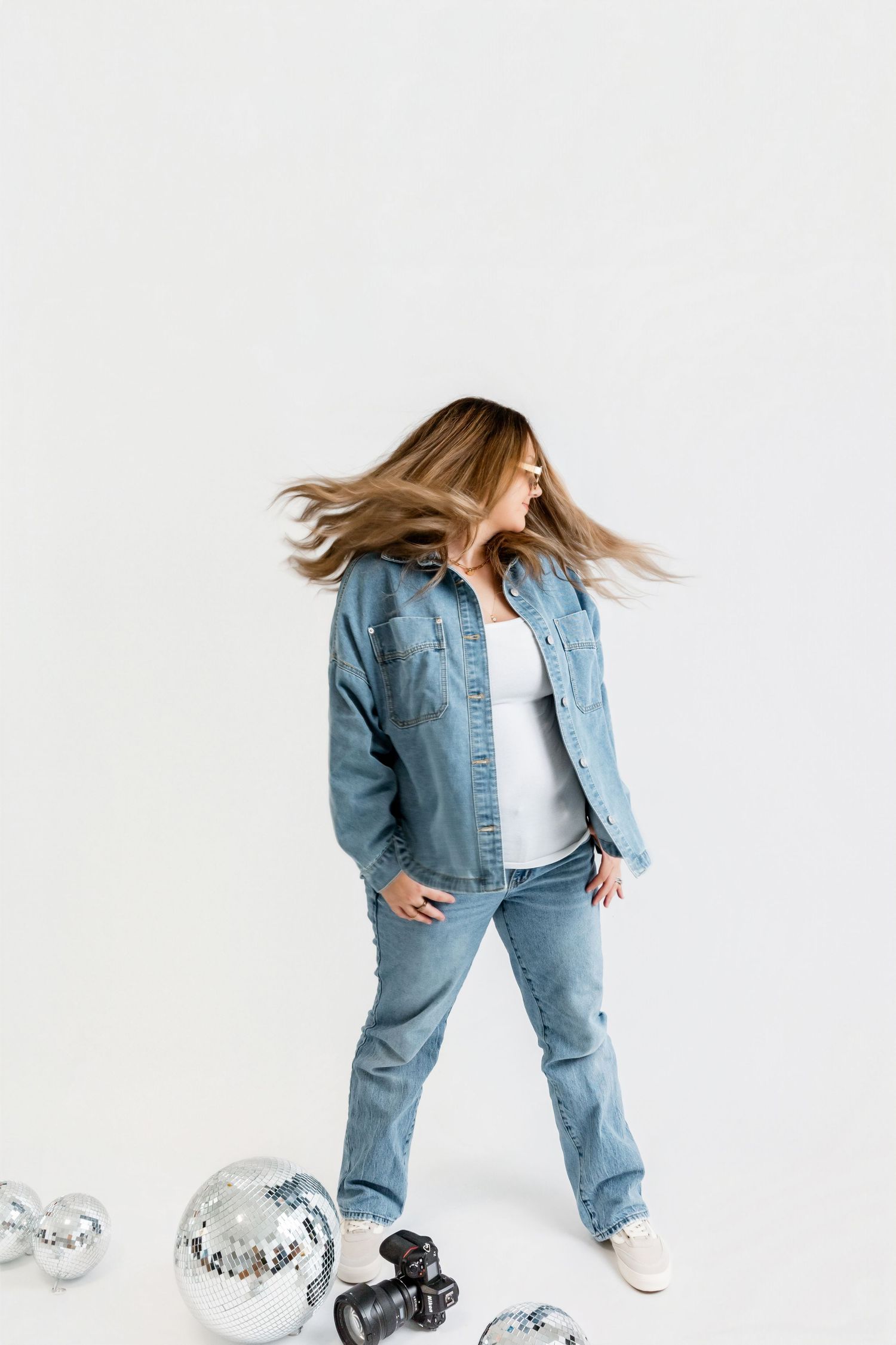 Person in light-wash denim outfit strikes dynamic poses against white background with sneakers and camera props.