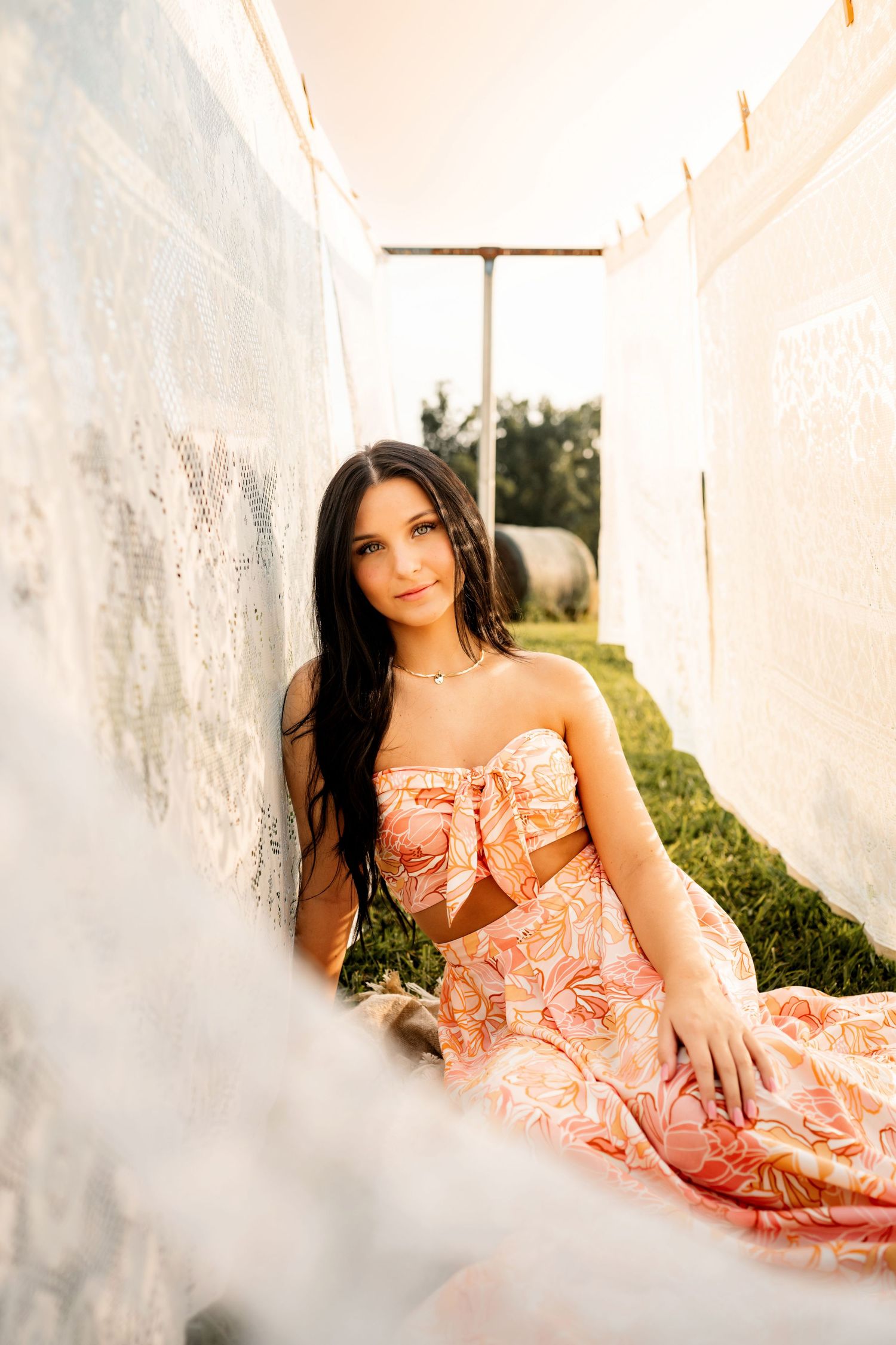 Woman in peach-colored dress reclines gracefully during golden hour photoshoot.