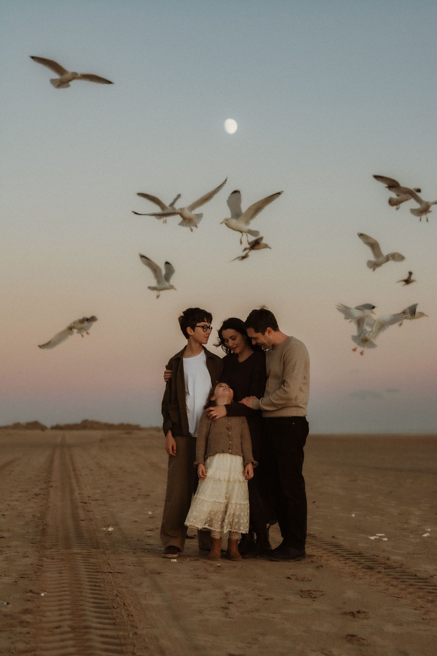 a family standing on the beach while being surrounded by flying birds