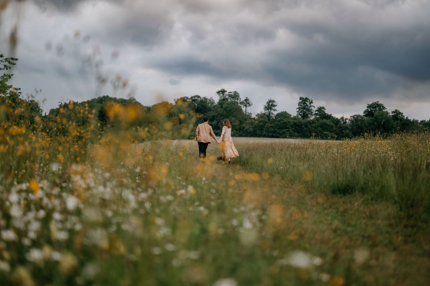 A couple holding hands while walking away in a field of wild flowers