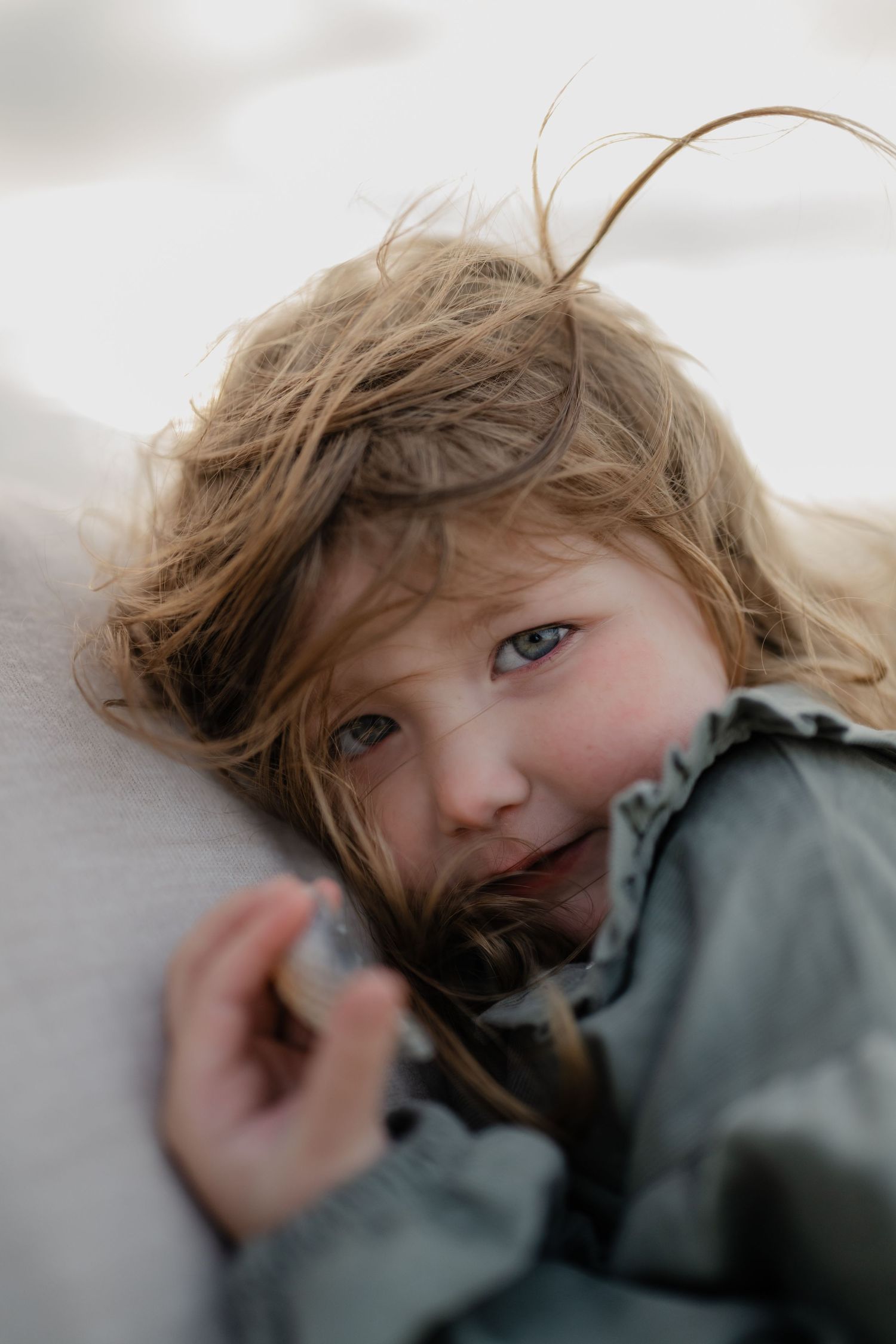 a little girl with blue eyes looking inti the camera lens while keeping her head close to her dad's chest at a photo session in Camber sands