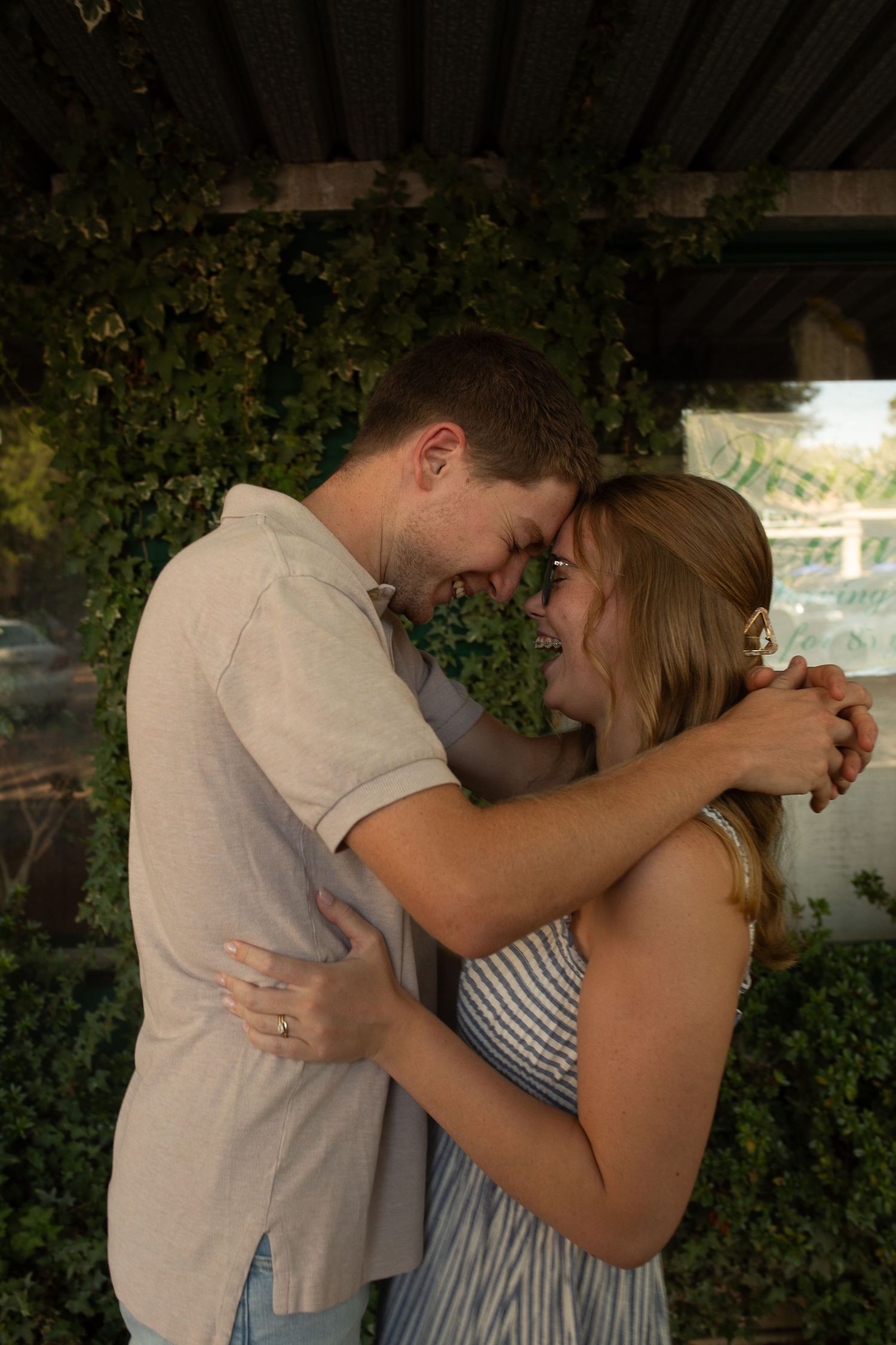 A couple shares an intimate moment in front of a green foliage backdrop.