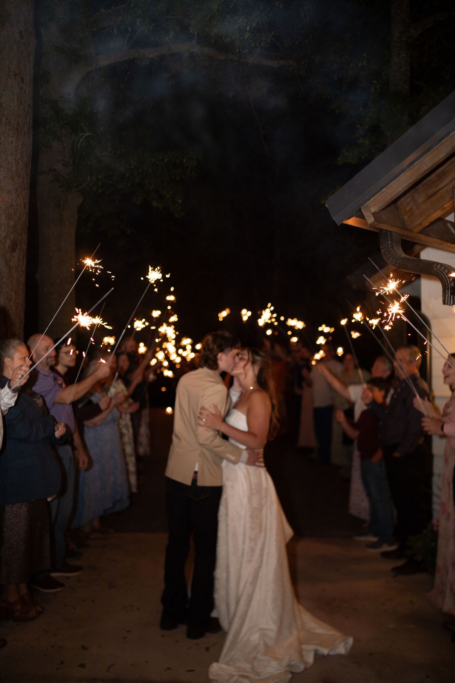 A bride and groom share a kiss during a romantic sparkler send-off at their outdoor evening wedding reception.