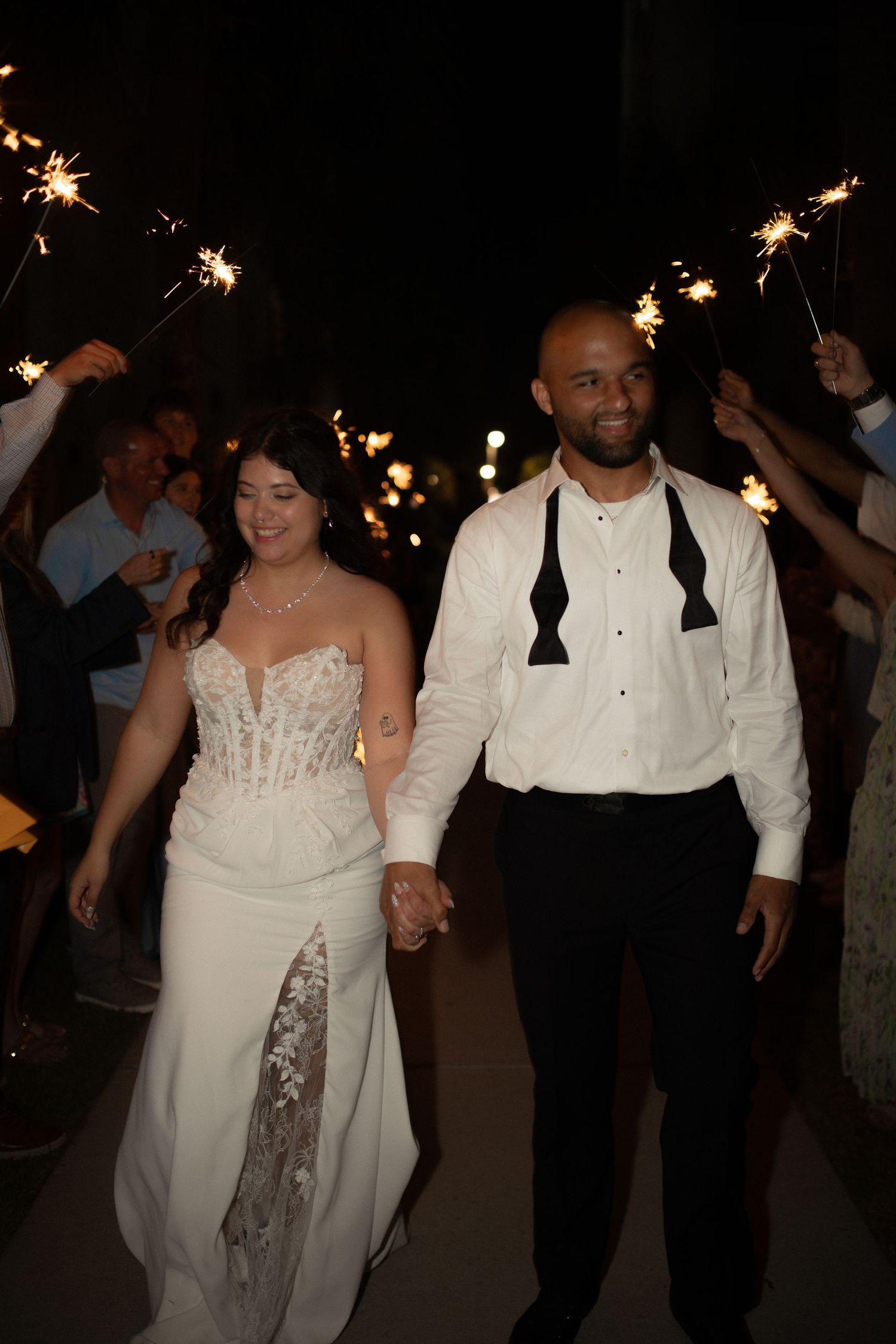Bride and groom walk through sparkler exit at night wedding reception, holding hands in elegant attire.